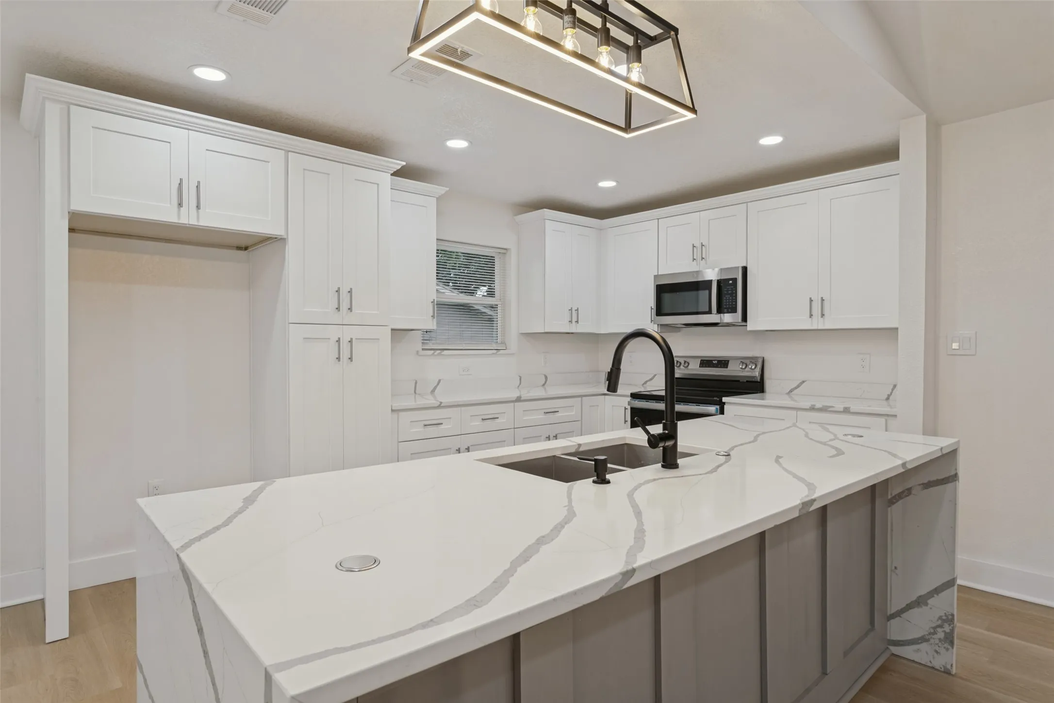 Kitchen featuring a large island with a double basin sink and black faucet, white shaker cabinets, stainless steel appliances, and recessed lighting