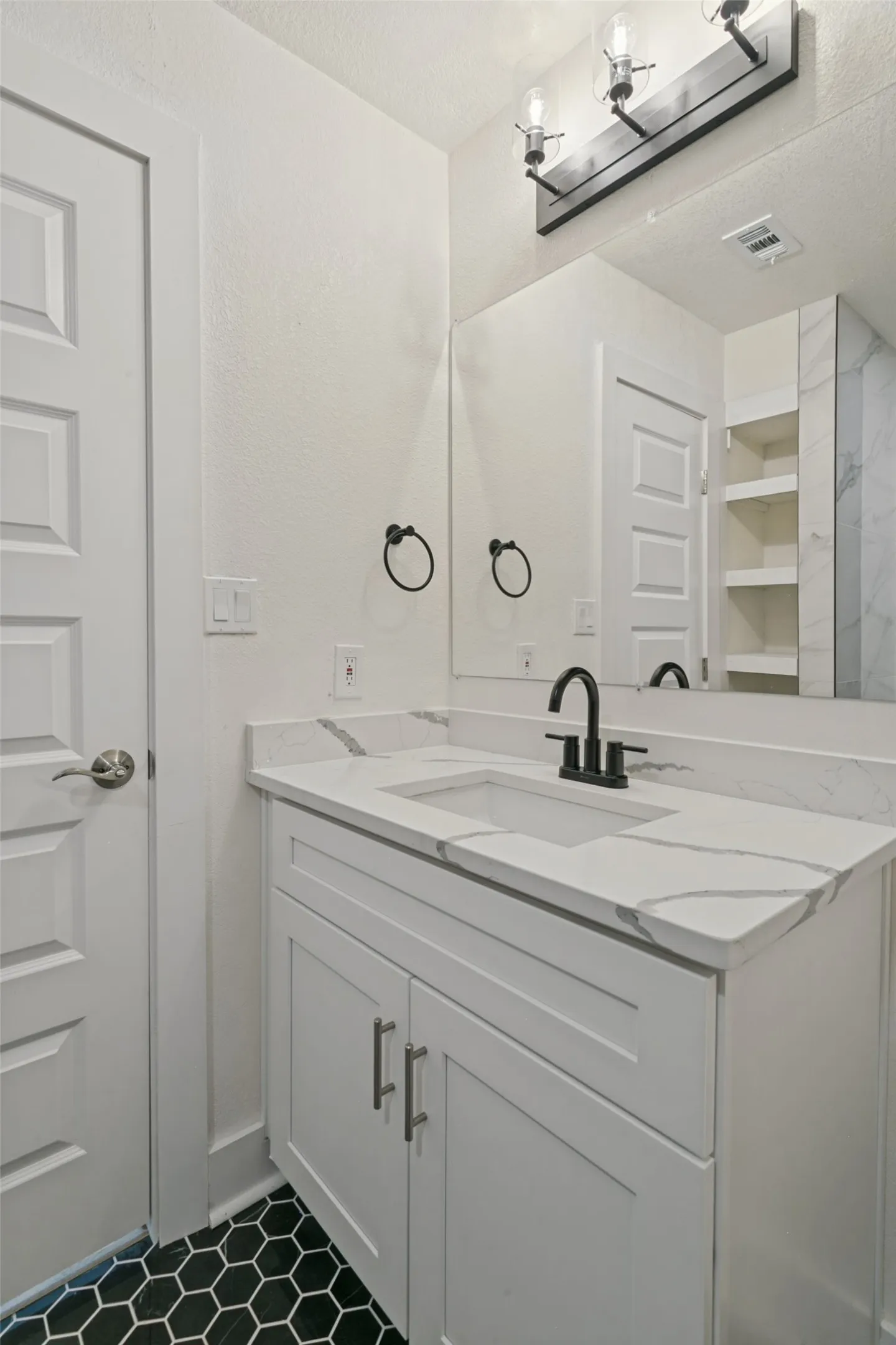 White shaker-style vanity with a quartz countertop, integrated sink, and black hexagonal floor tiles