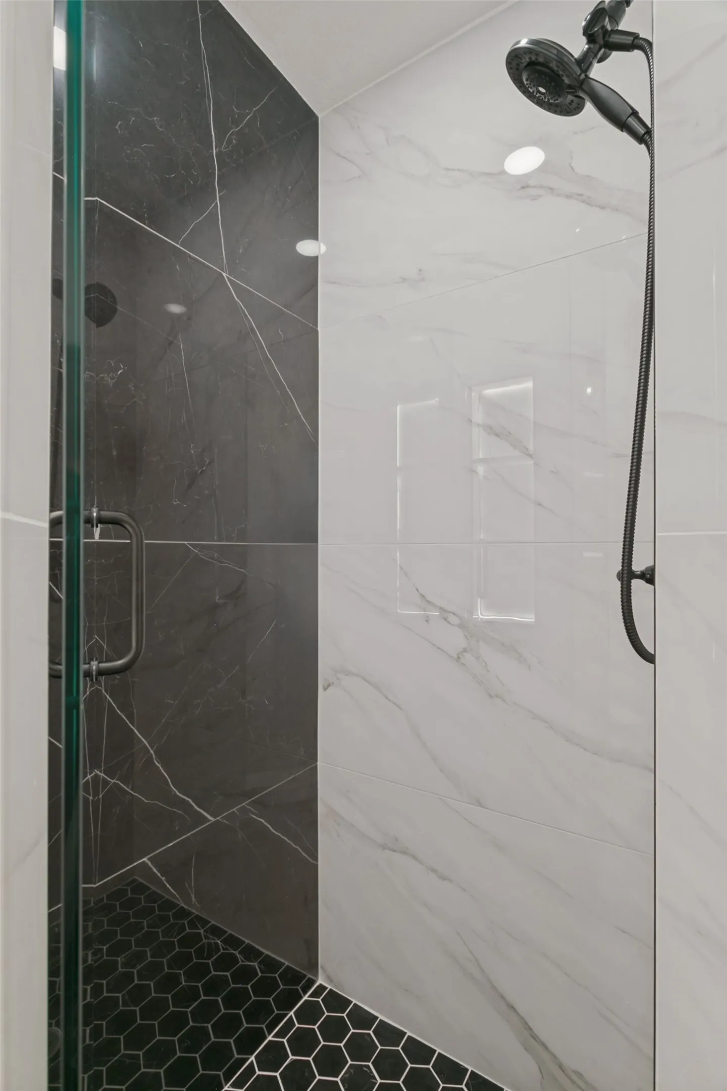 Shower enclosure with a glass door, dark hexagonal floor tiles, and a multi-setting showerhead