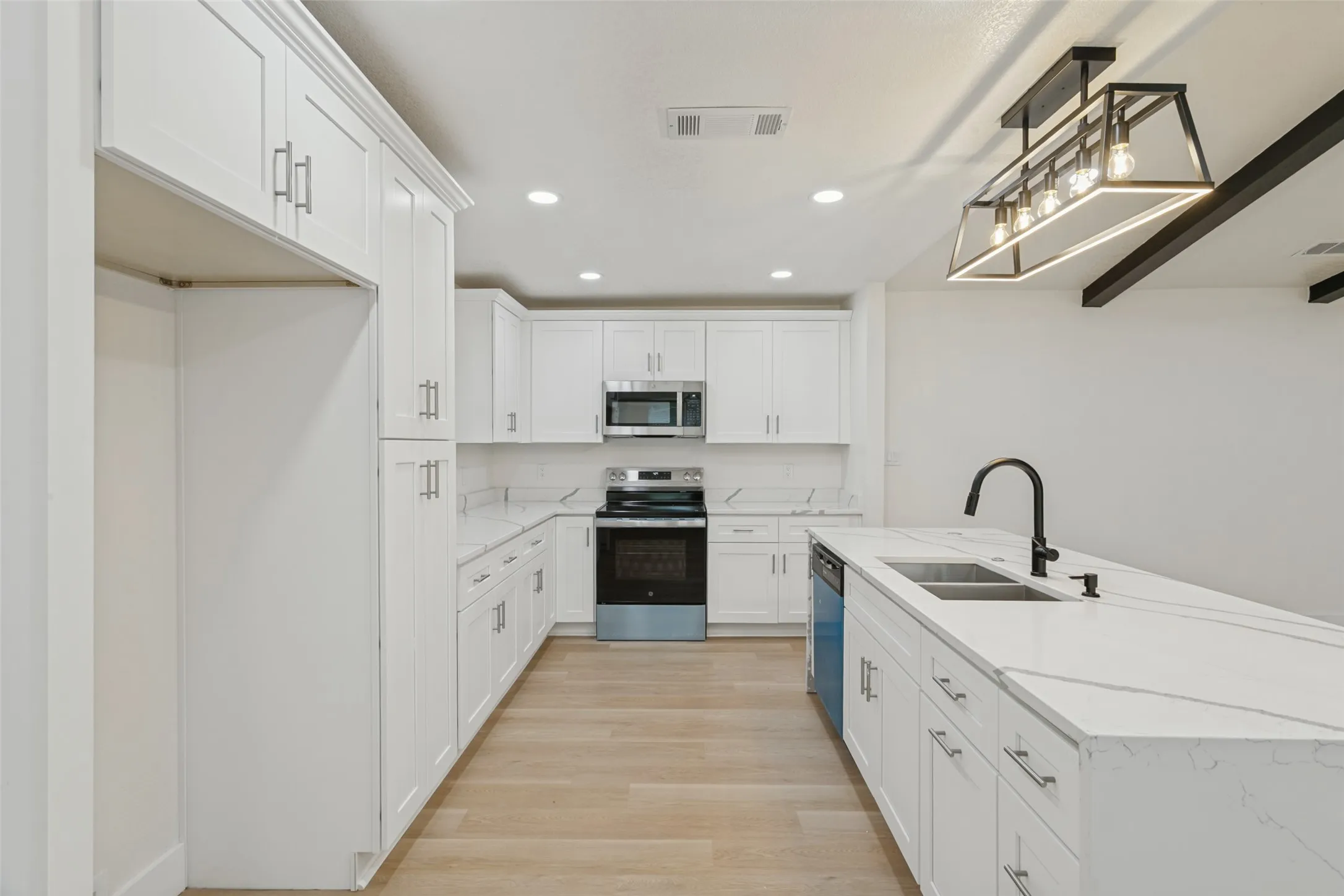 Kitchen featuring extensive white cabinetry, light wood-finish flooring, white countertops, stainless steel appliances, and an island with an undermount sink and black faucet