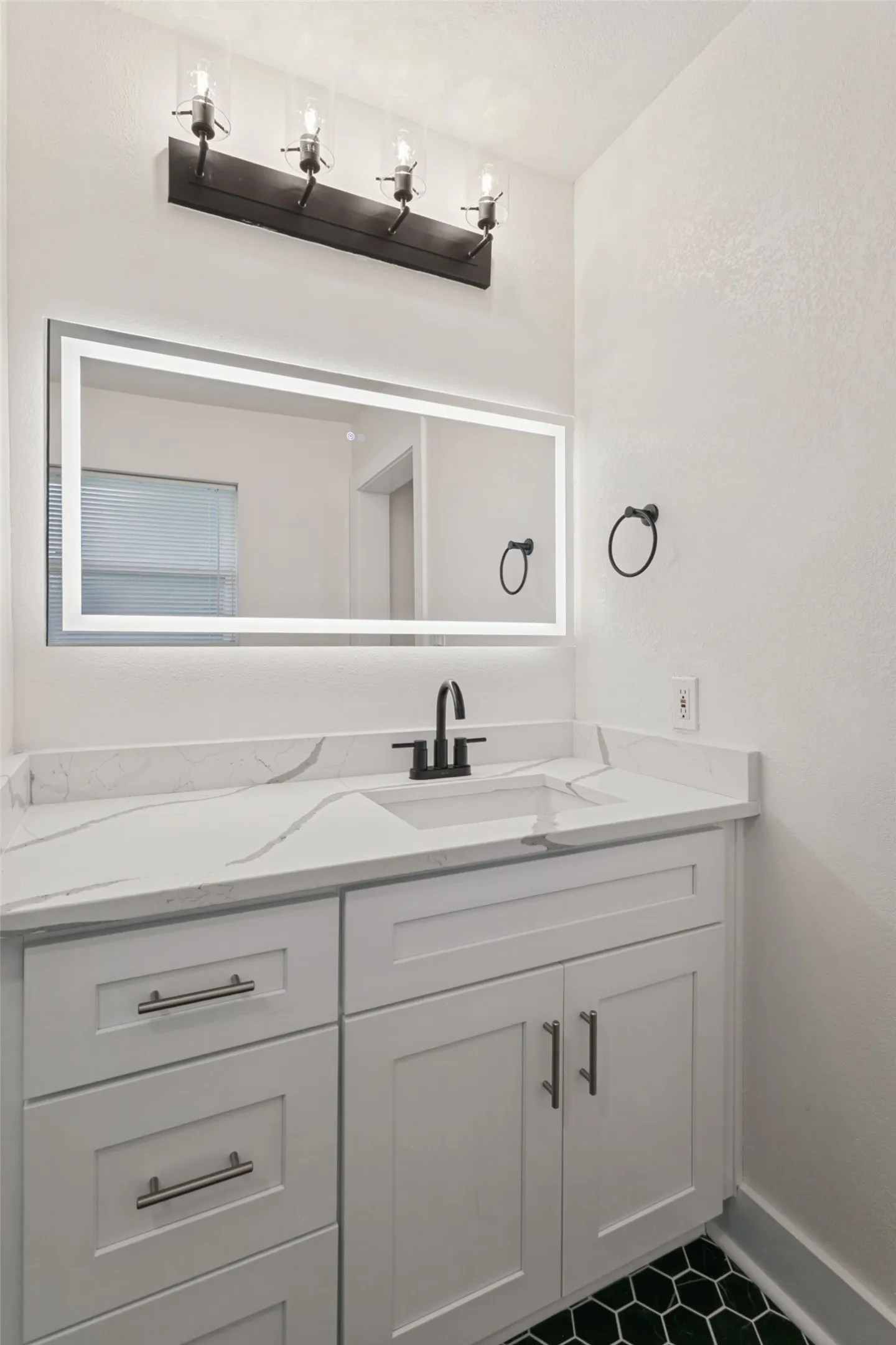 White vanity with shaker-style cabinetry, quartz countertop, and integrated sink