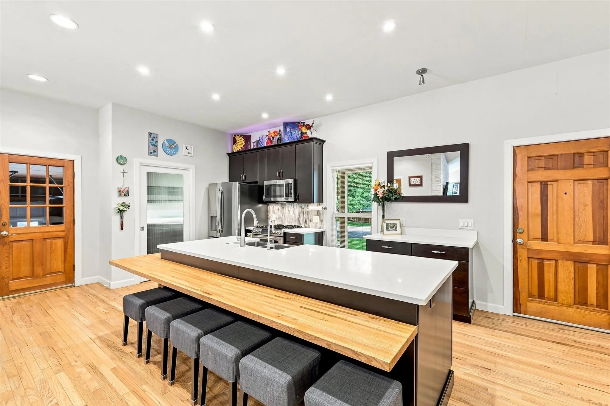 Kitchen featuring an island with quartzite countertops, butcher block bar seating, recessed lighting, rich cabinetry, stainless steel appliances (including a double oven gas range), and wood flooring.