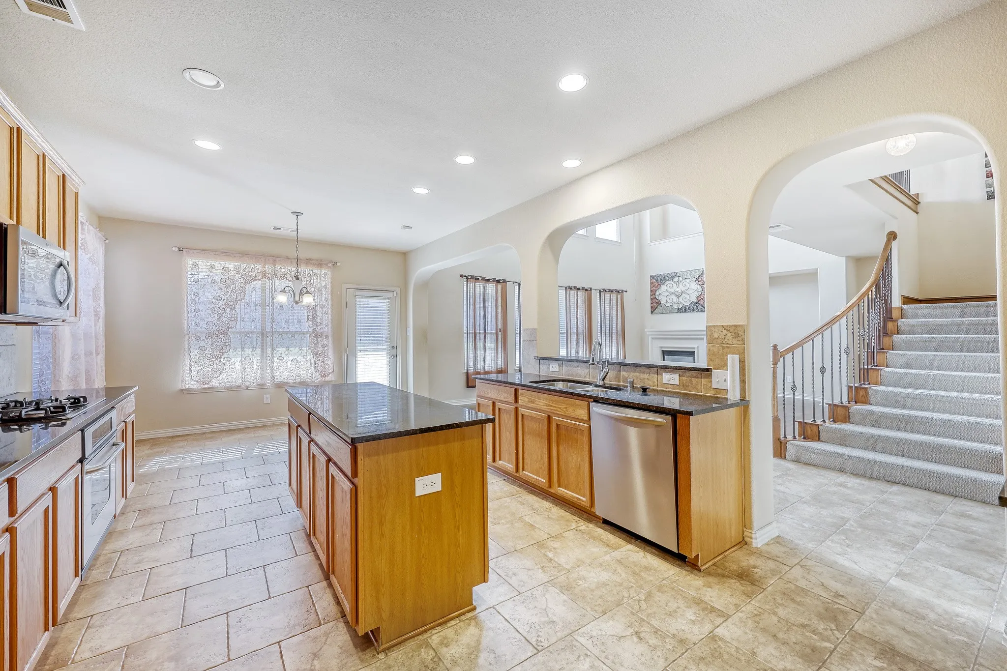 Kitchen featuring wood cabinetry, black countertops, stainless steel appliances, and tile flooring