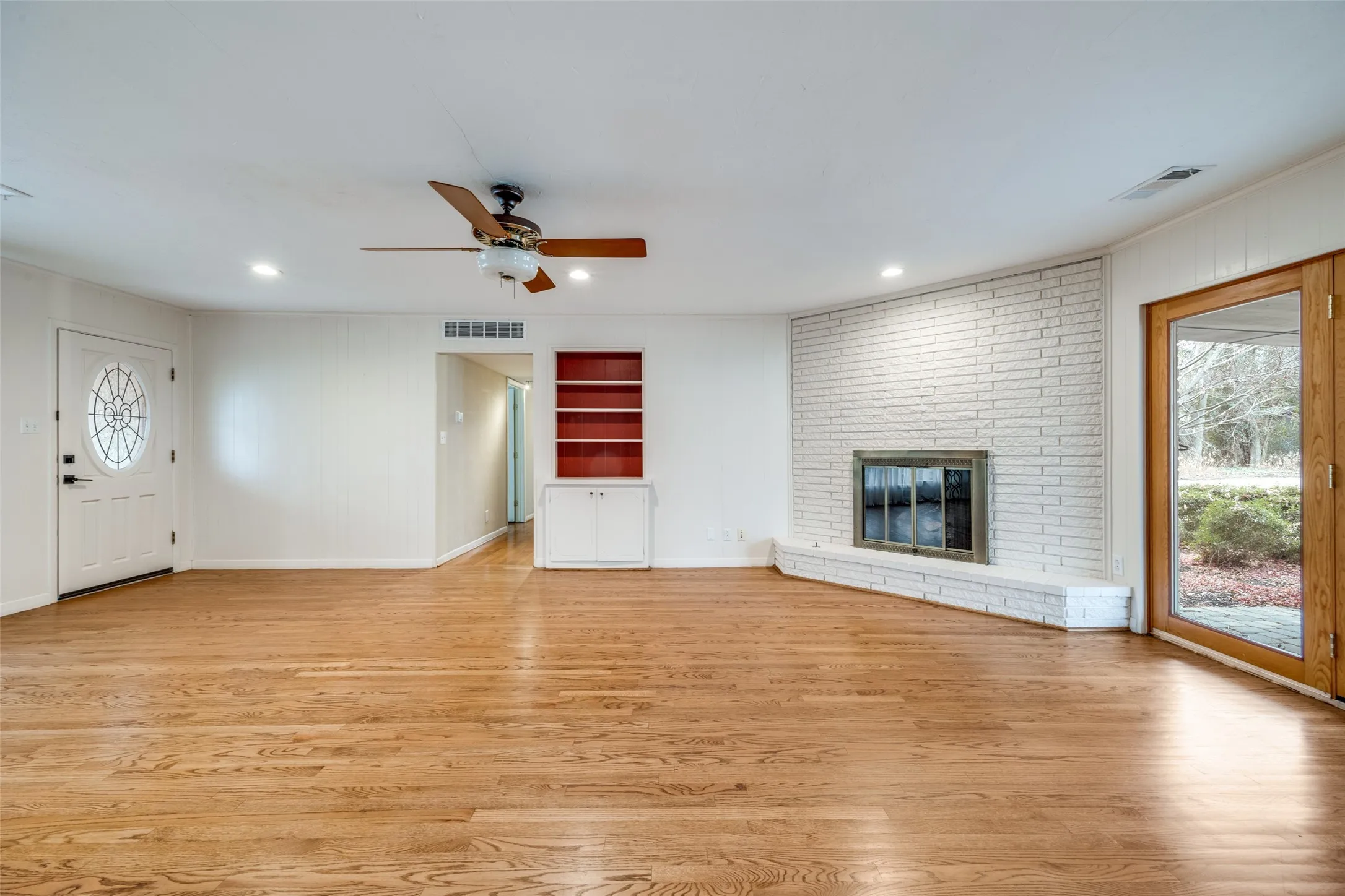 Hardwood flooring, painted brick fireplace, built-in shelving, glass-paned double doors, and recessed lighting