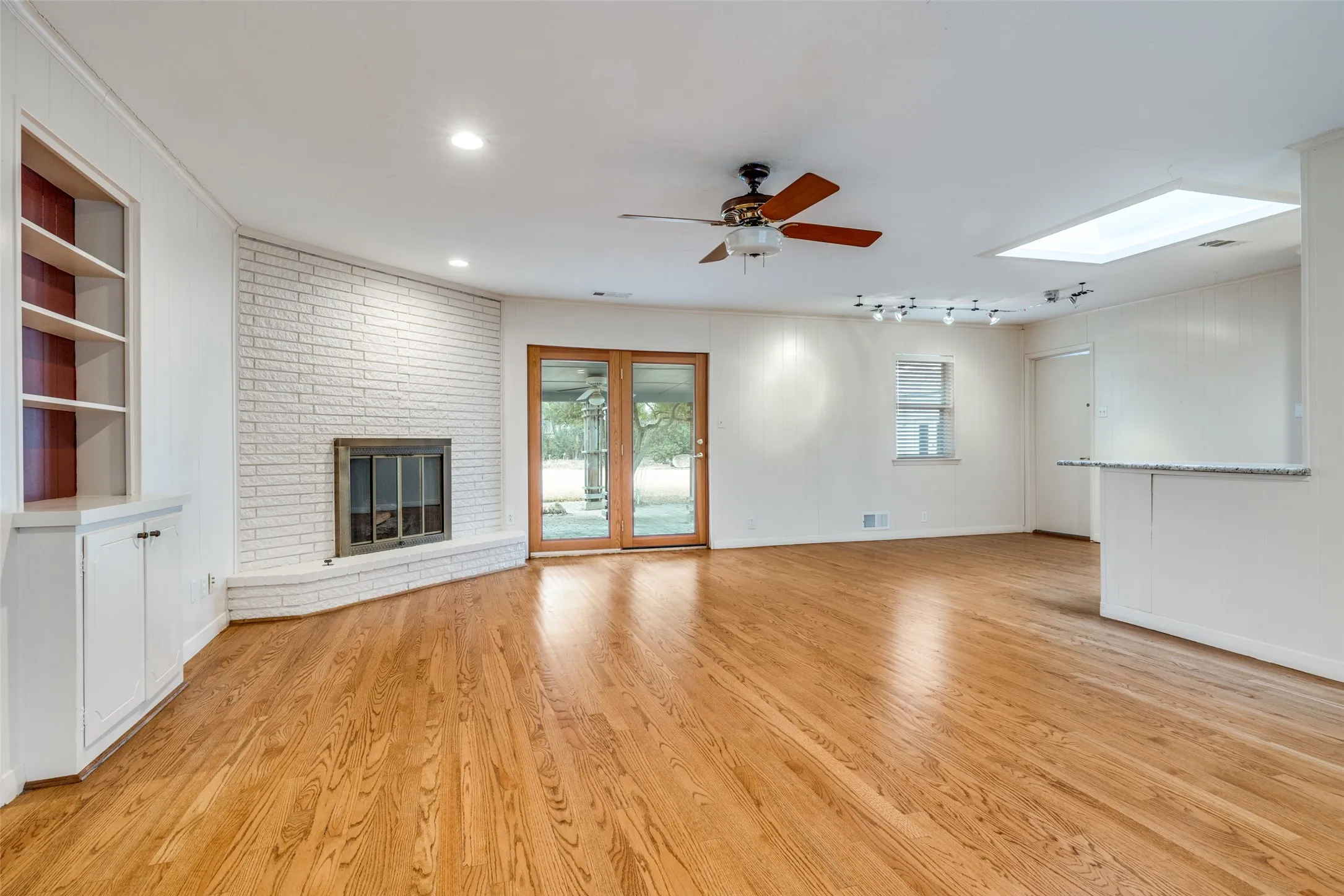 Hardwood flooring, fireplace, built-in shelving, glass-paned double doors, and a ceiling-mounted skylight