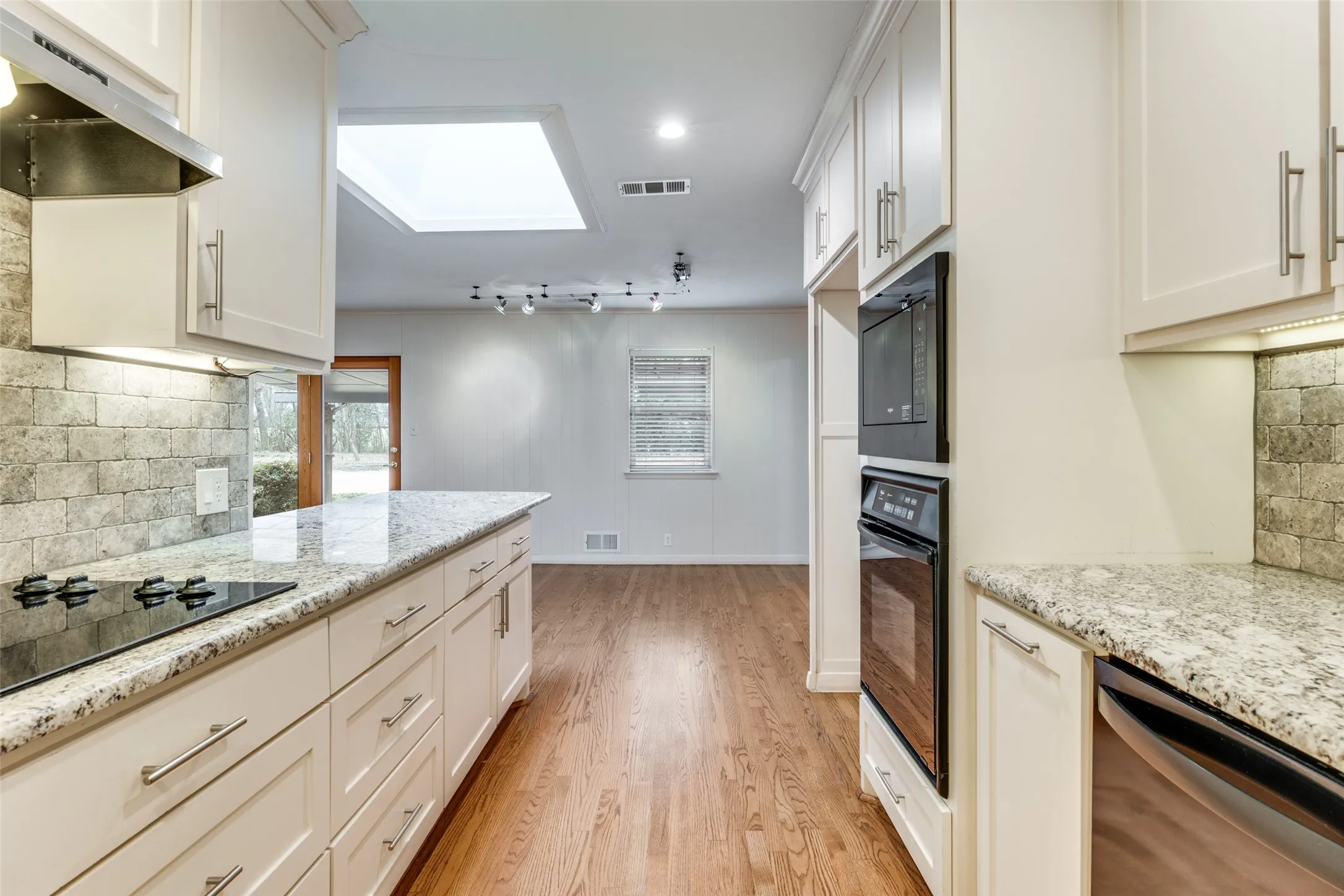 Kitchen featuring white cabinetry, light-toned countertops, stone backsplash, built-in oven and microwave.