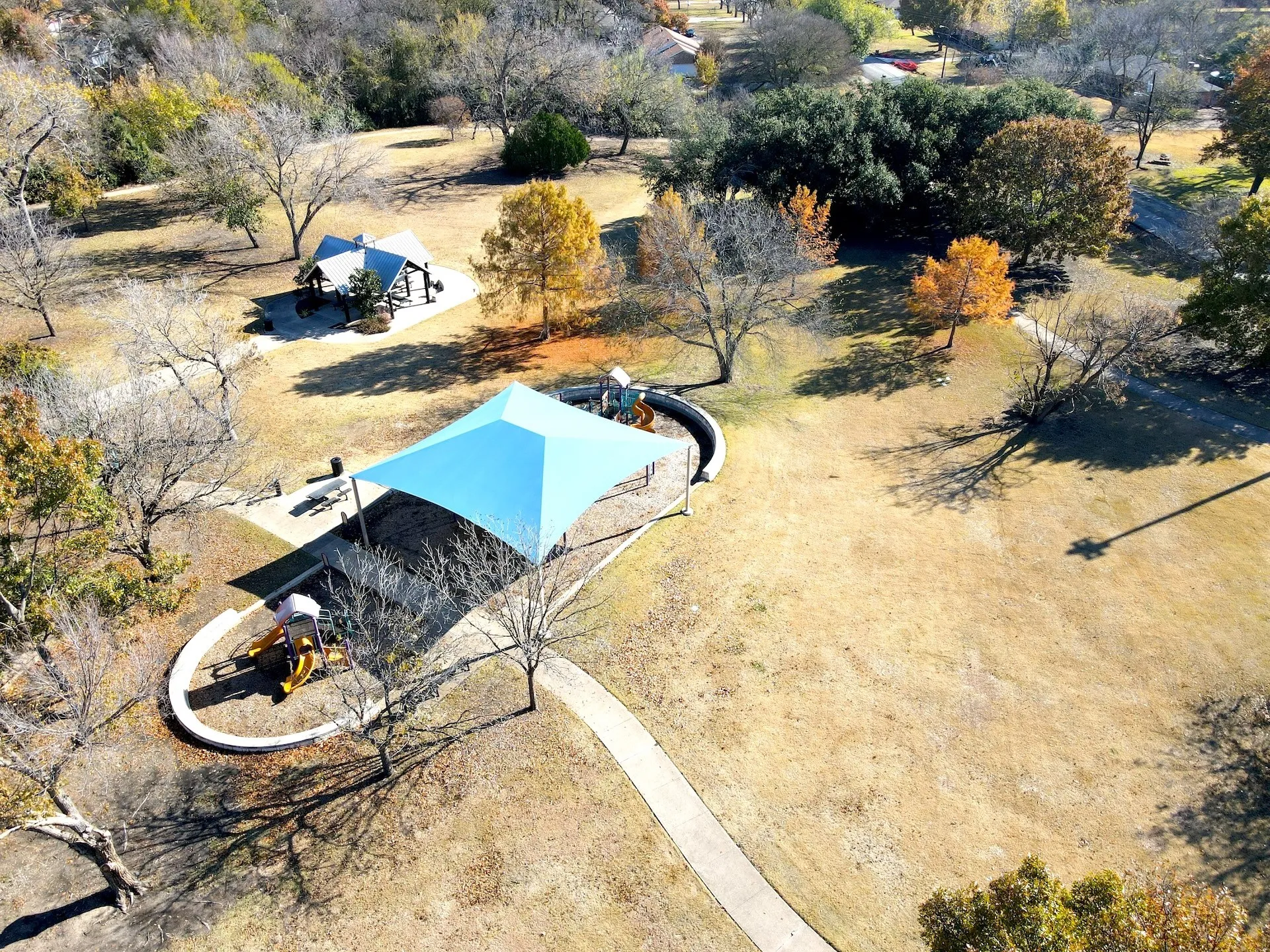 Expansive park area featuring established trees, walking paths, and two covered recreation structures