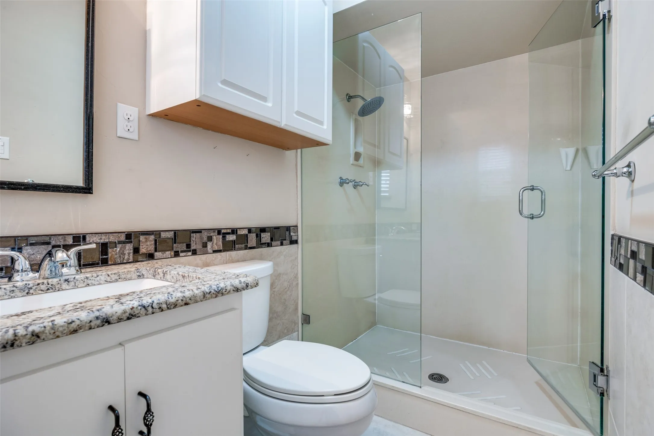 Granite-finish vanity countertop with an undermount sink, mosaic tile backsplash, frameless glass shower enclosure, and a chrome rain shower head