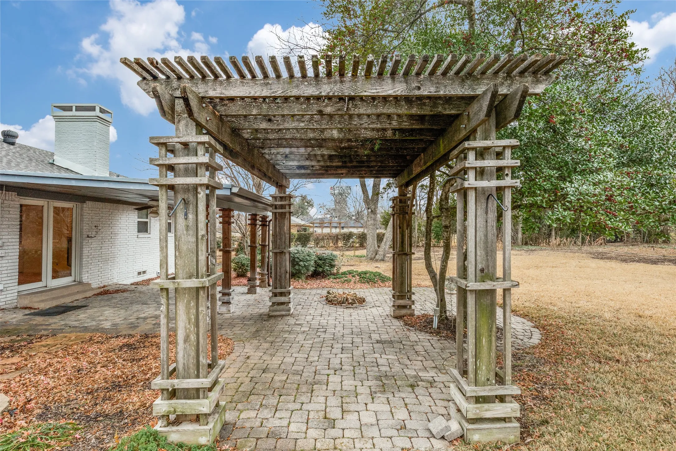 Expansive outdoor living area featuring a wooden pergola, brick paver patio, and mature landscaping