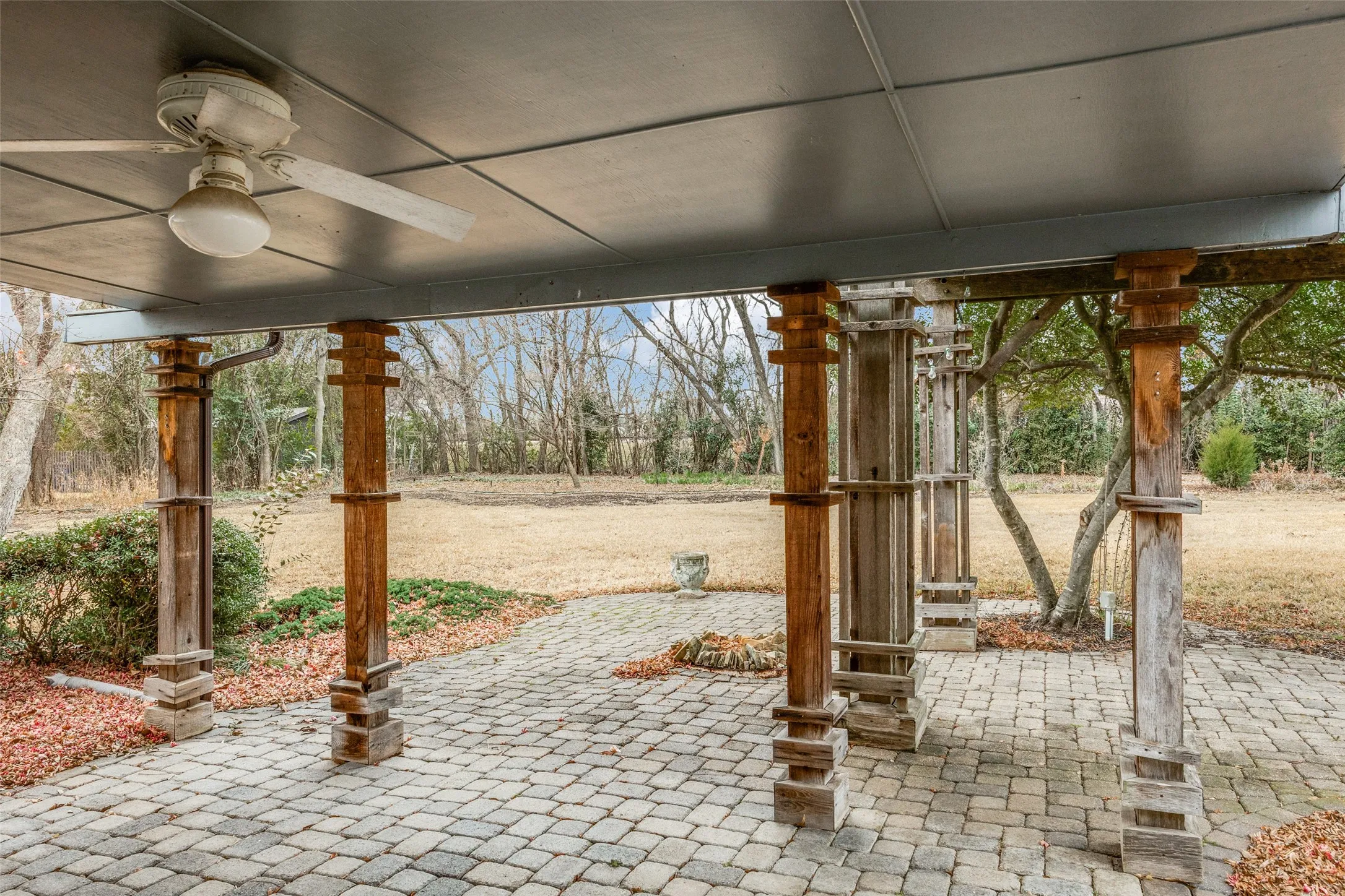Covered outdoor space featuring a ceiling fan, wood support pillars, and a paver patio