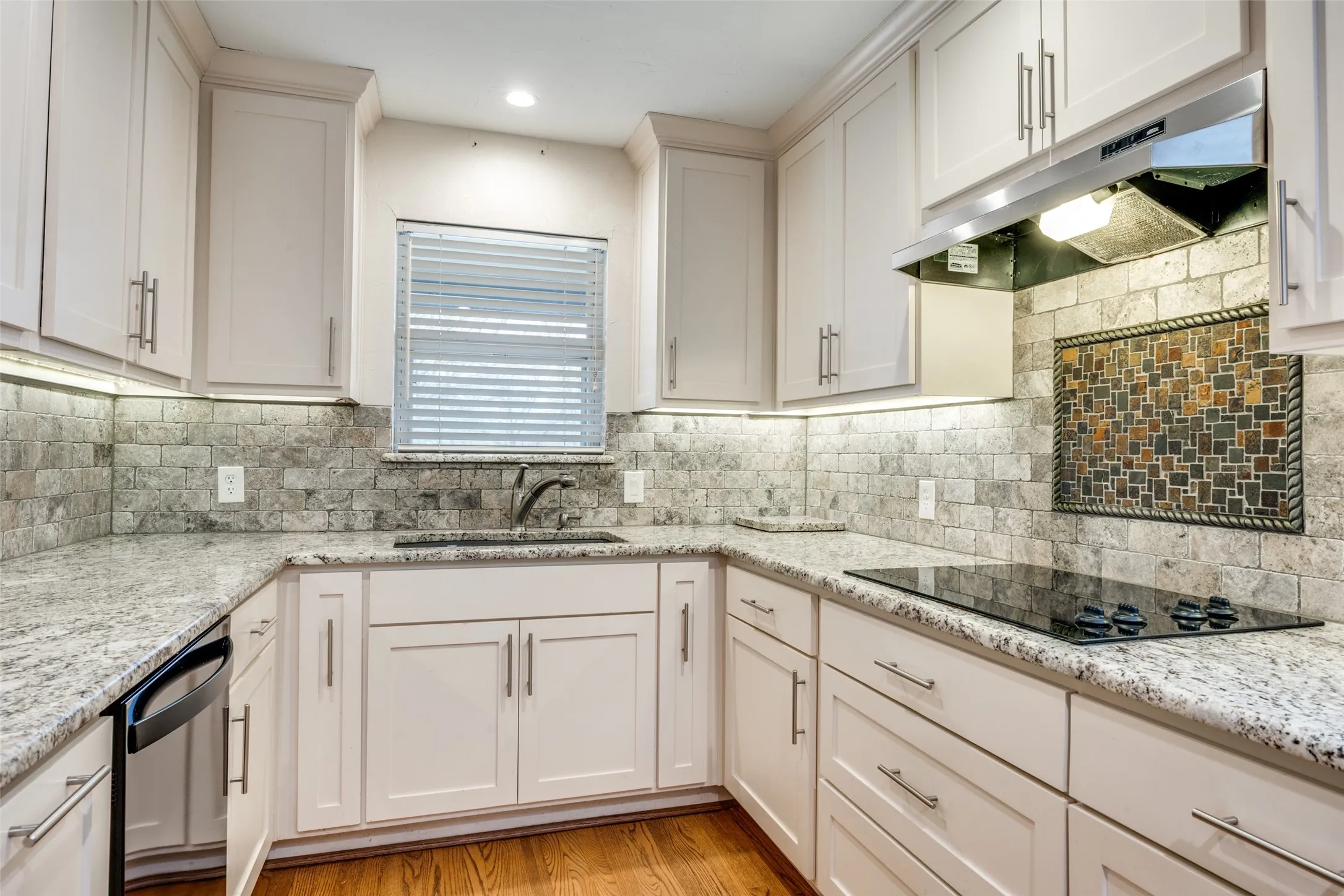 Kitchen featuring light-toned cabinetry, granite countertops, Stone backsplash, and a built-in cooktop