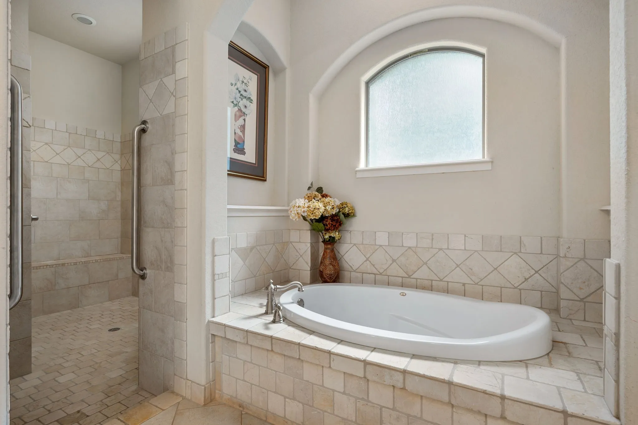 Tile-surround soaking tub with deck-mounted faucet, walk-in shower with tiled walls and flooring, and arched frosted window