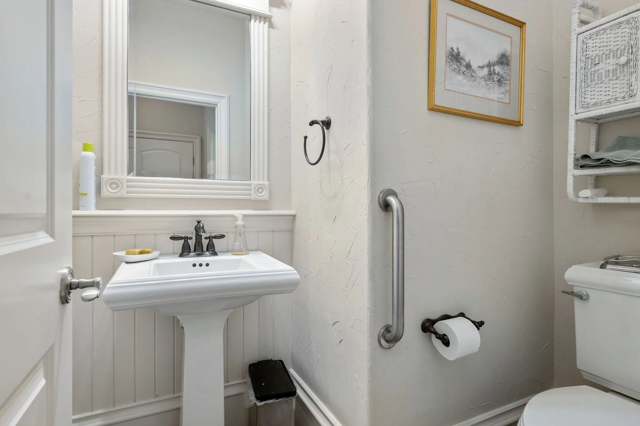 Pedestal sink with dark-toned fixtures, framed mirror, and beadboard wainscoting