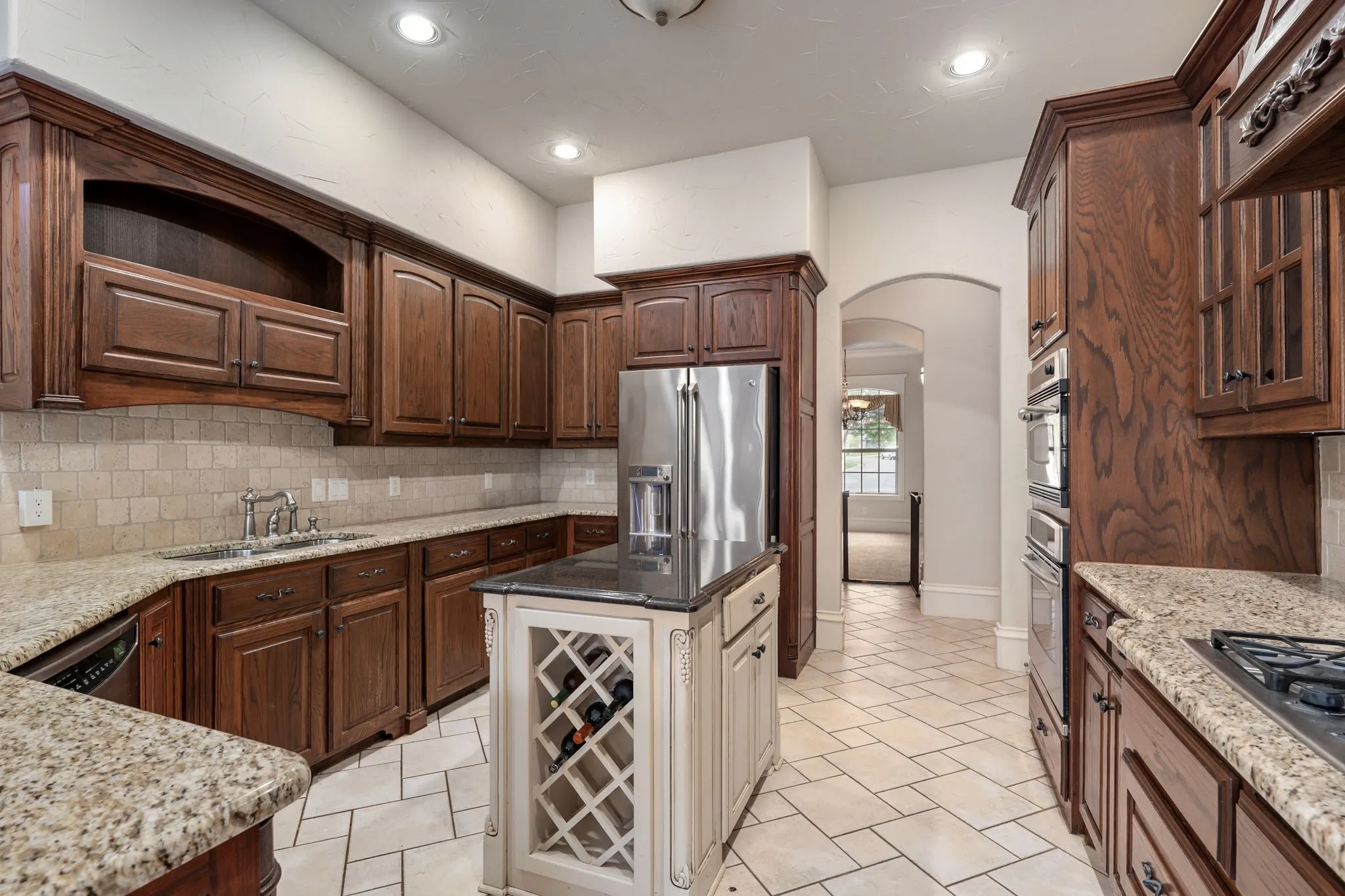 Kitchen featuring extensive wood cabinetry, stone countertops, stainless steel appliances, a tiled backsplash, and a central island with a built-in wine rack
