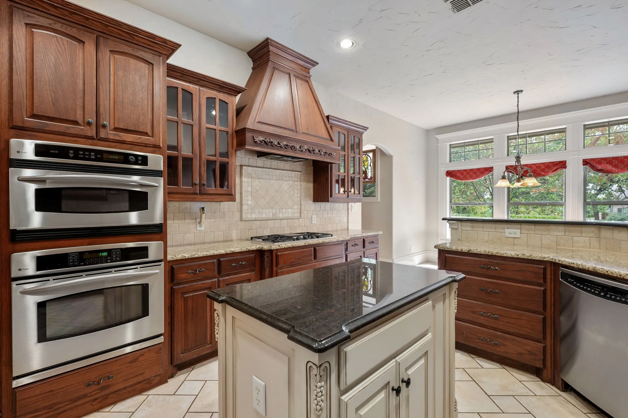 Kitchen featuring wood cabinetry, stainless steel double wall ovens, a center island with a dark countertop, granite countertops, and tile flooring