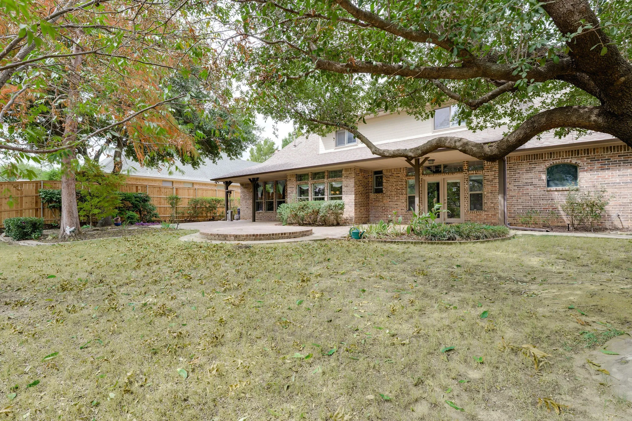 Expansive backyard featuring a red brick exterior, a covered patio with columns, a stone-finish patio, and mature trees