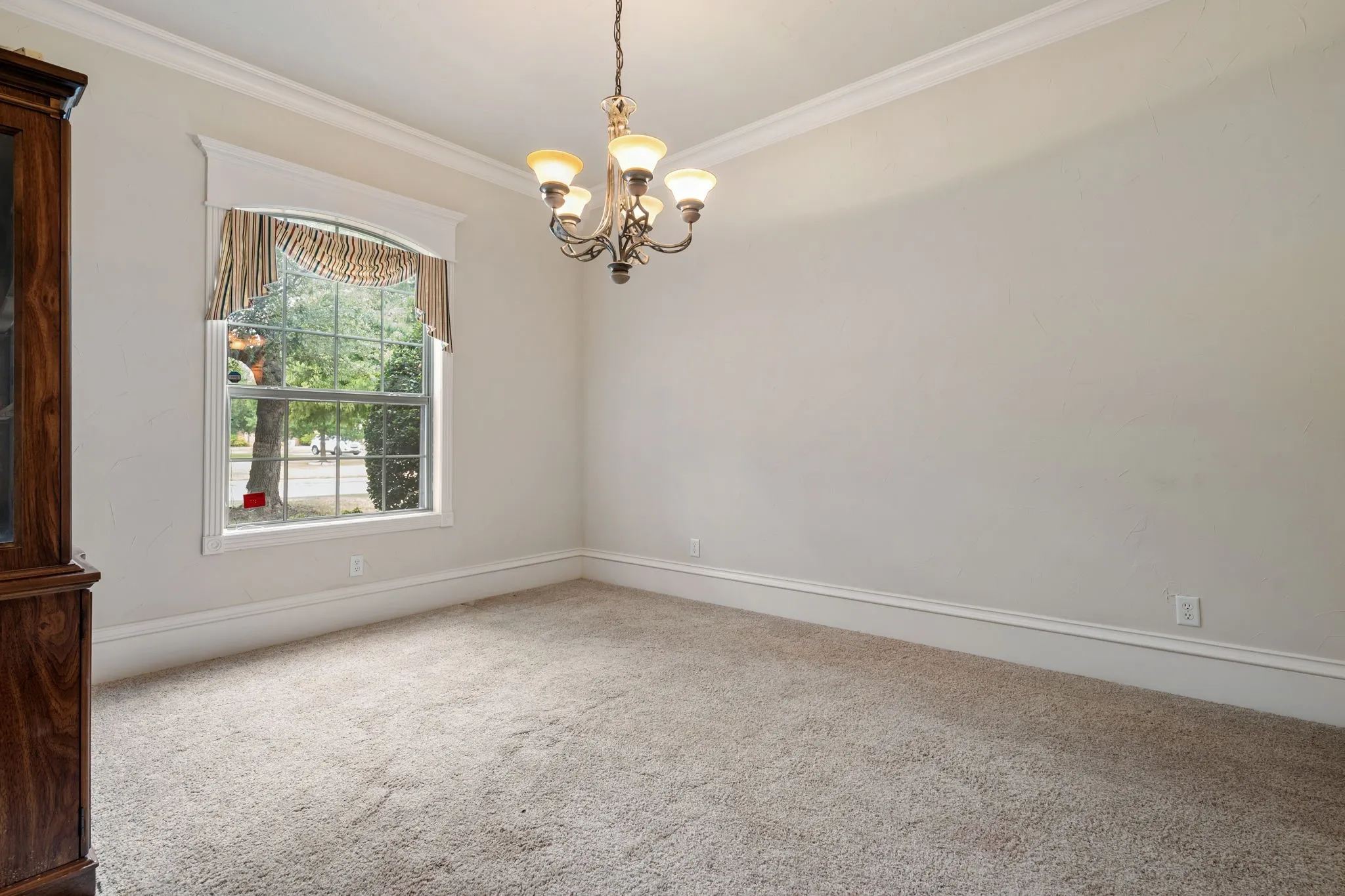 Crown molding, neutral wall color, carpeted flooring, and a decorative chandelier