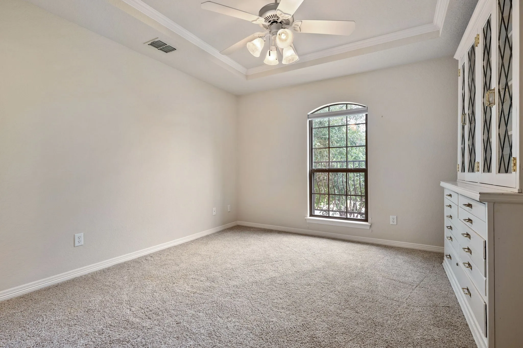 Tray ceiling with crown molding, ceiling fan, arched window, and neutral carpeting