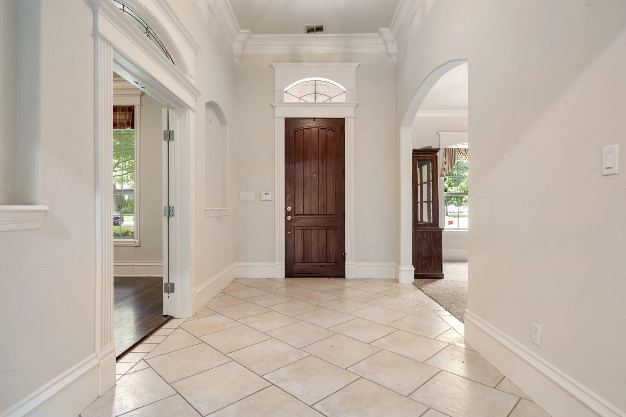 Tiled flooring, arched doorways, decorative moldings, wood-finish entry door, and transom window