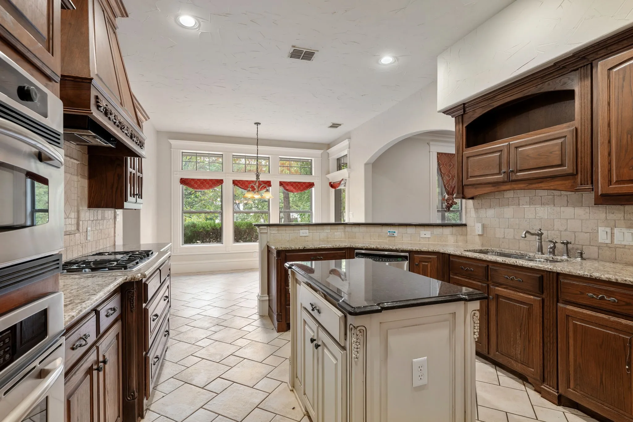 Kitchen featuring wood cabinetry, light-toned tile flooring, granite countertops, a built-in oven, and a centered island