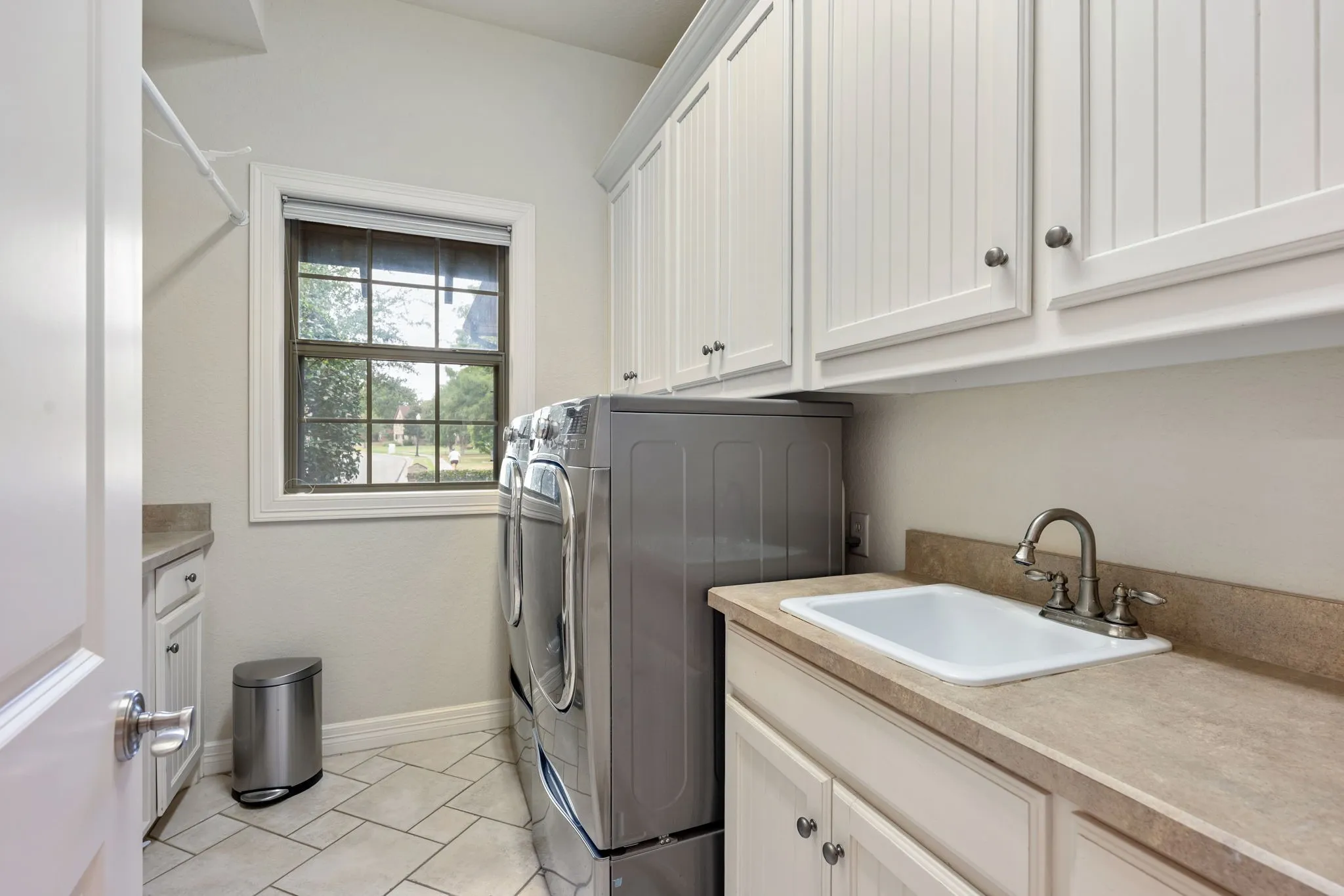 Laundry room featuring extensive white cabinetry, a utility sink with a faucet, light-toned countertop, and tiled flooring