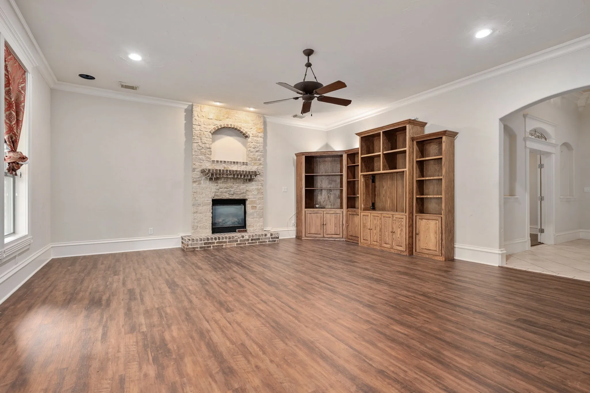 Wood-finish flooring, stone-clad fireplace with brick hearth, built-in wooden cabinetry, recessed lighting, and a ceiling fan