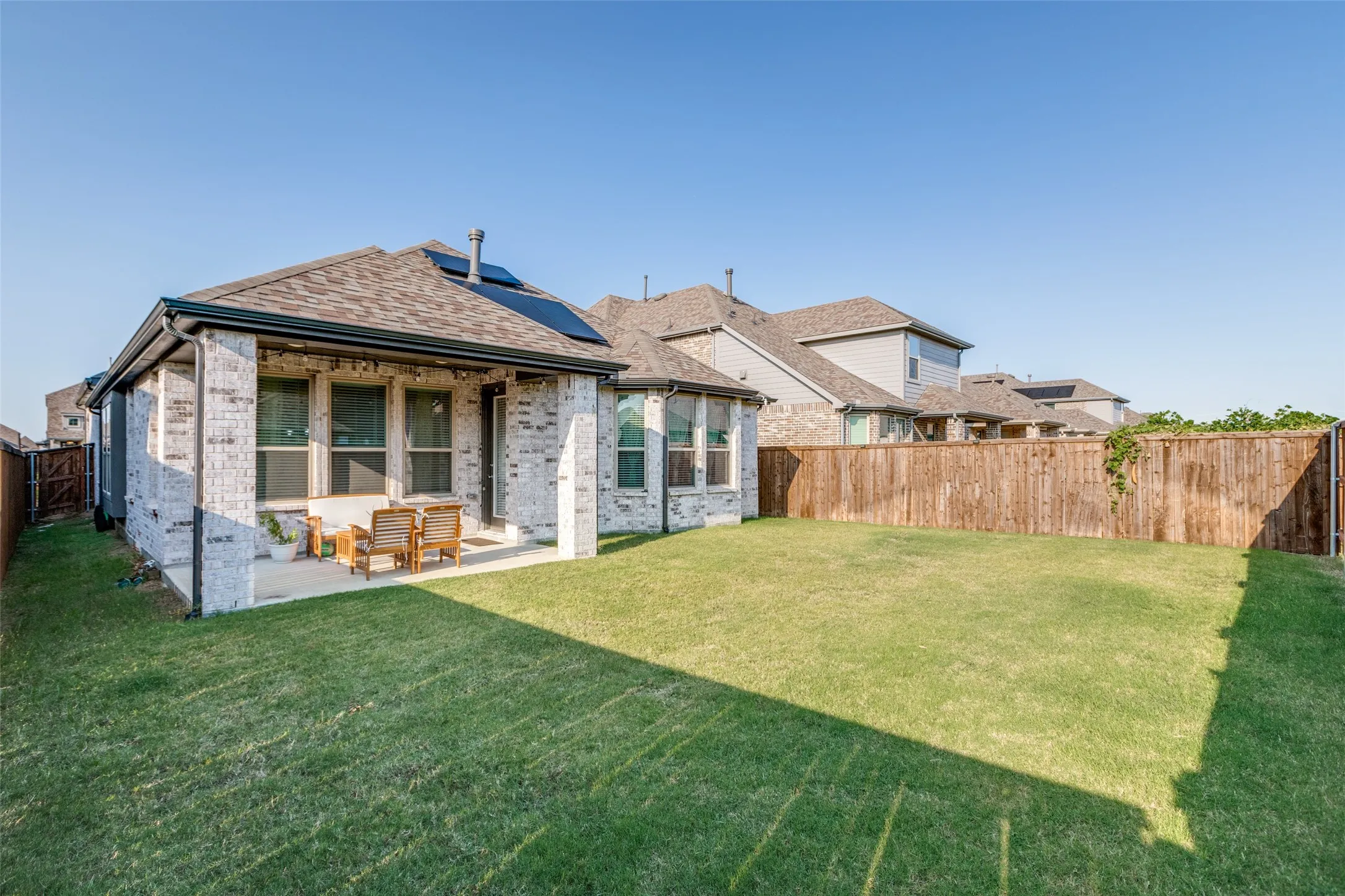 Rear view of property featuring a fenced backyard, a patio area, brick siding, solar panels, and outdoor lounge area