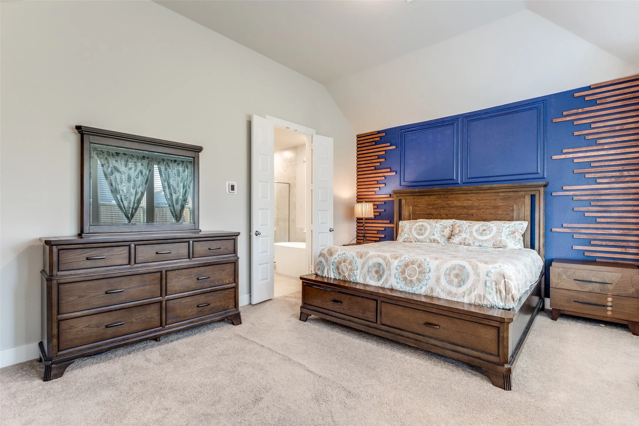 Bedroom with light colored carpet, ensuite bathroom, and lofted ceiling