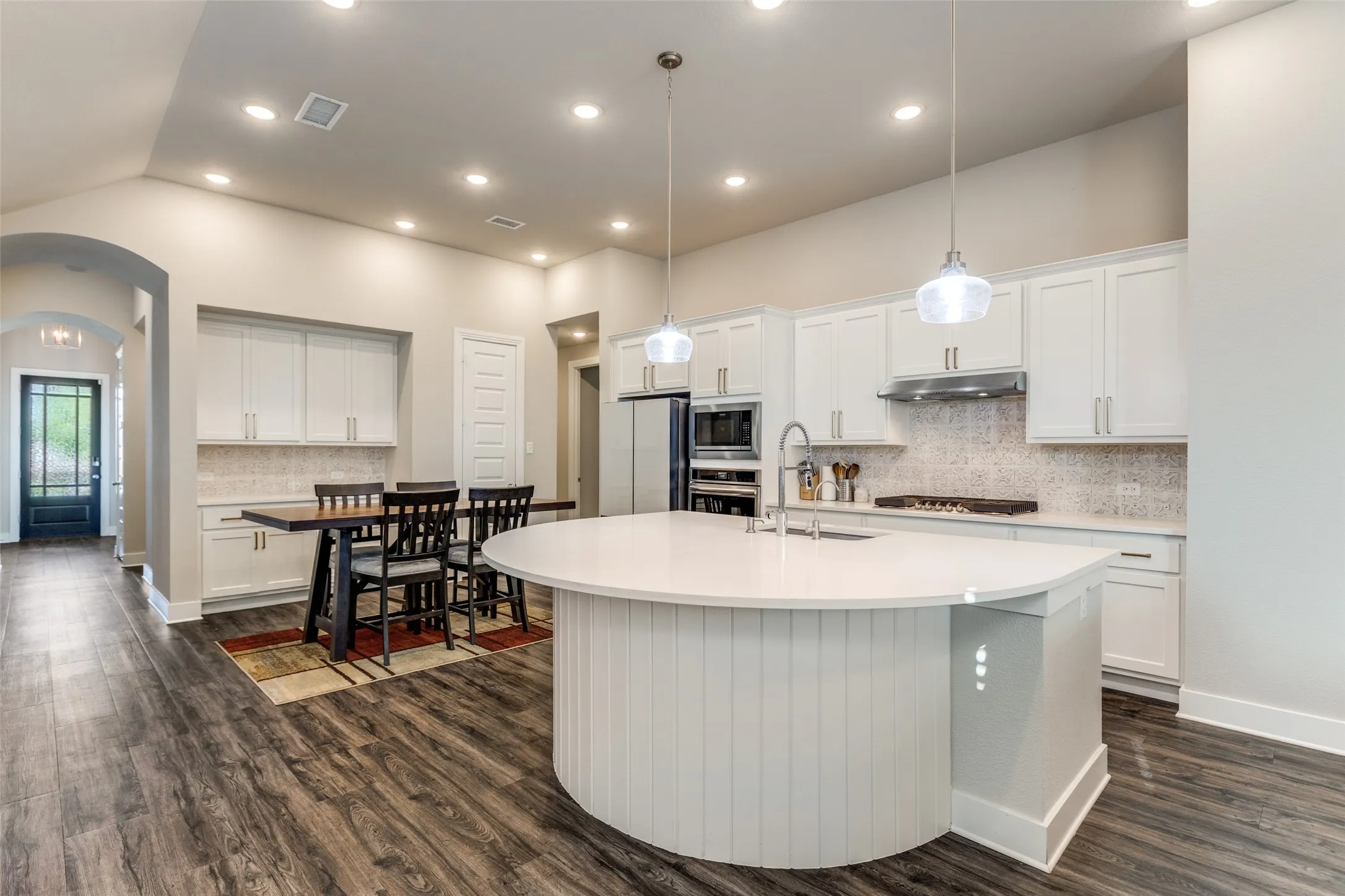 Kitchen with decorative backsplash, white cabinetry, pendant lighting, arched walkways, and recessed lighting