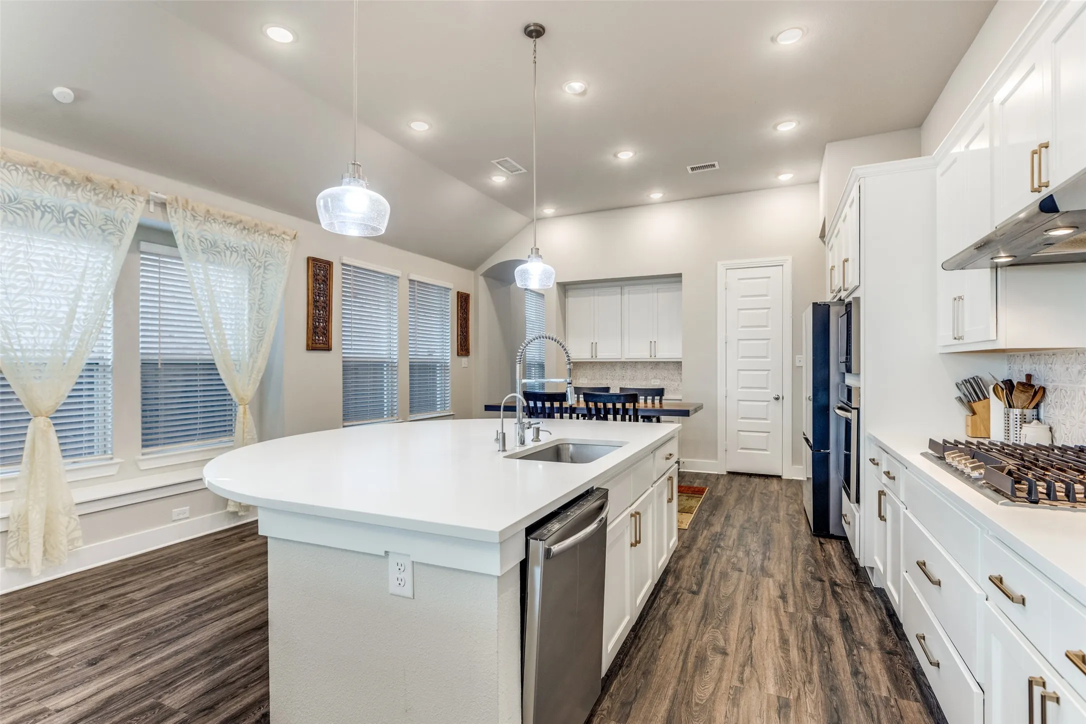 Kitchen with dark wood-style flooring, white cabinetry, backsplash, a kitchen island with sink, and vaulted ceiling