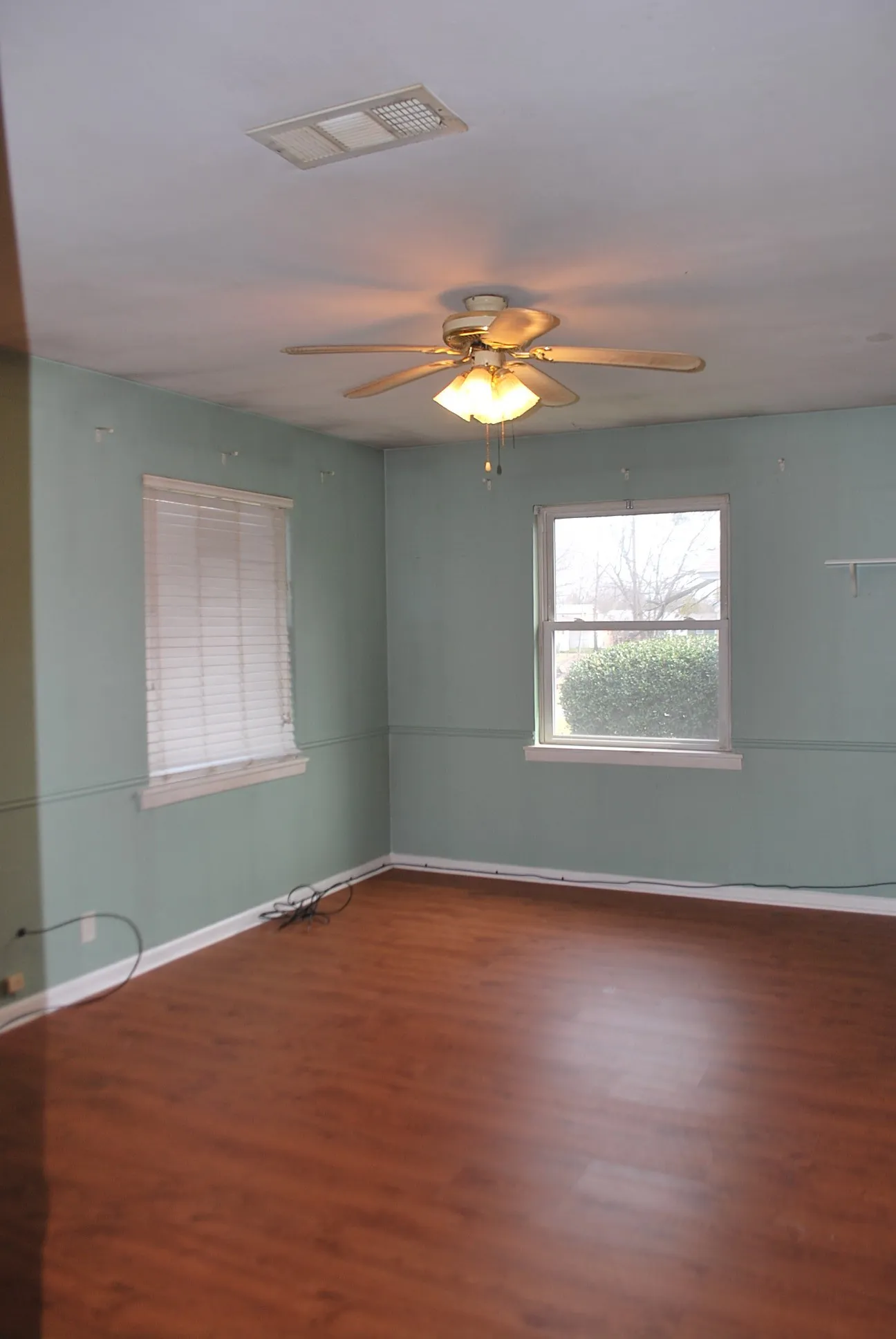 Wood-finish flooring with white trim, two windows, and a ceiling fan with integrated lighting