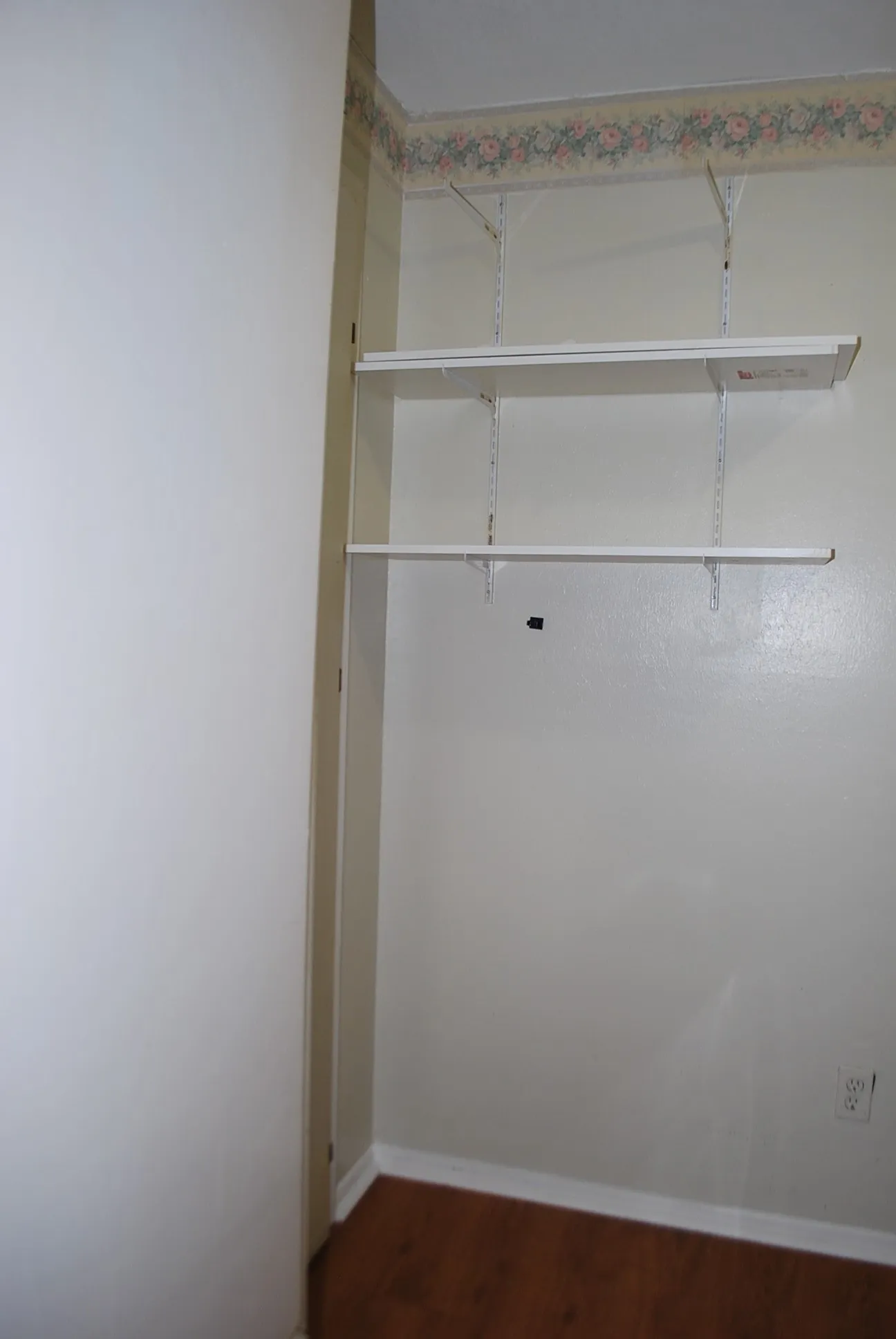 Adjustable shelving system with two white shelves, wood-finish flooring, and white trim