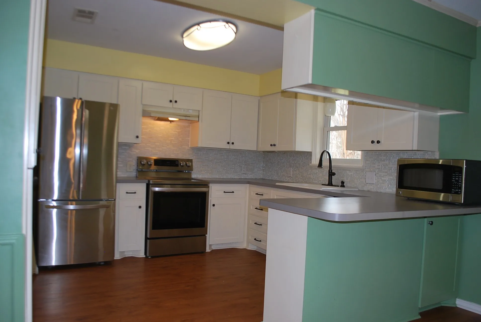 White cabinetry, stainless steel appliances, wood-finish flooring, undermount sink, and a tiled backsplash