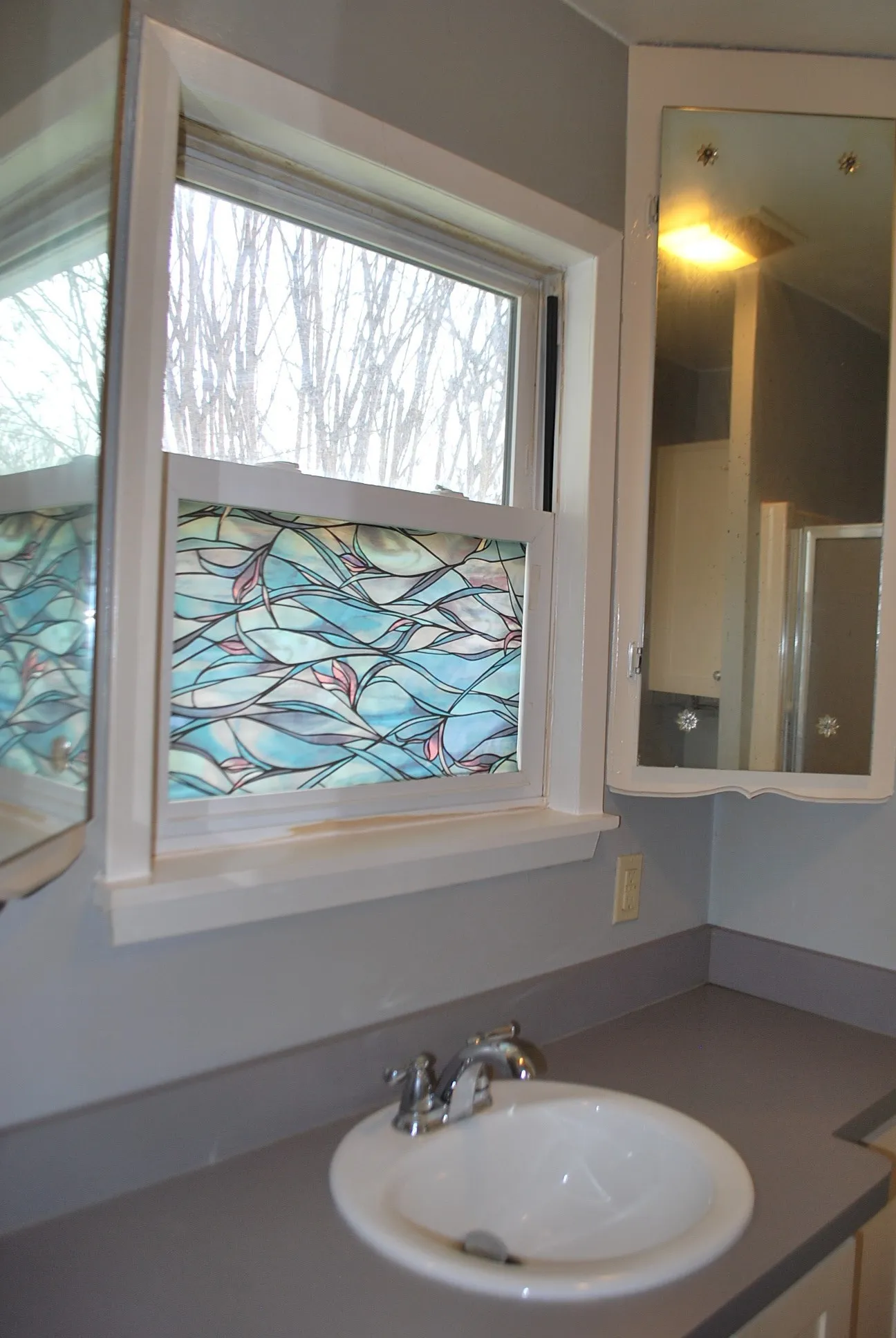Single vanity with integrated sink, chrome faucet, and a window with decorative film