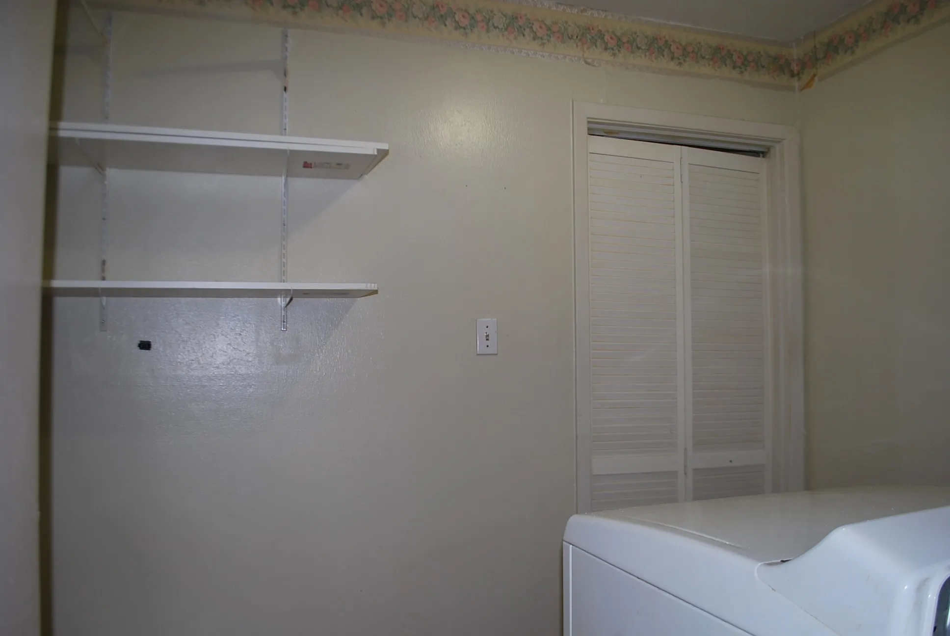 White louvered bi-fold closet doors, wall-mounted adjustable shelving, and a decorative wallpaper border
