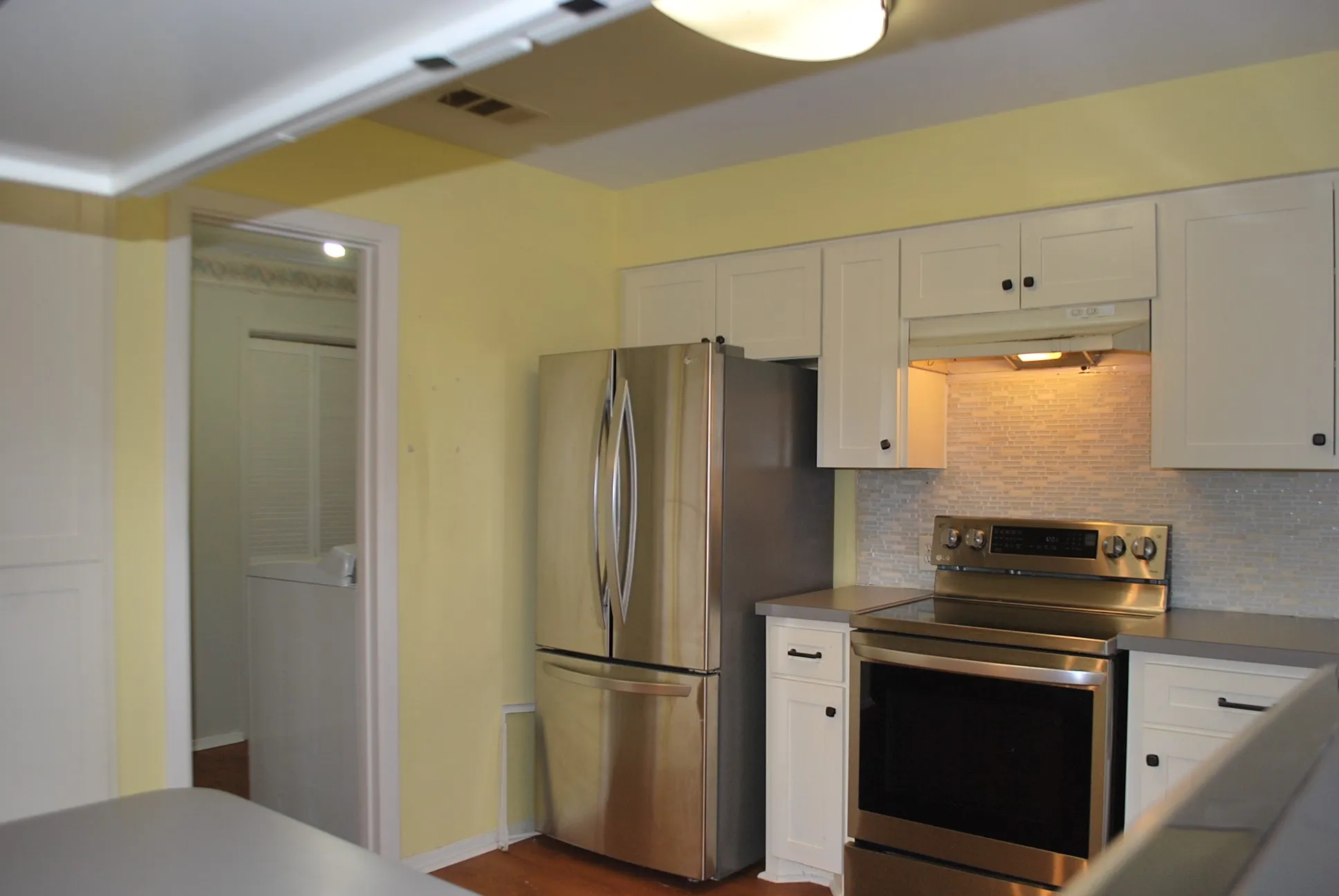 Stainless steel refrigerator, stainless steel range with overhead microwave hood, white cabinetry with dark hardware, gray countertop, and tile backsplash