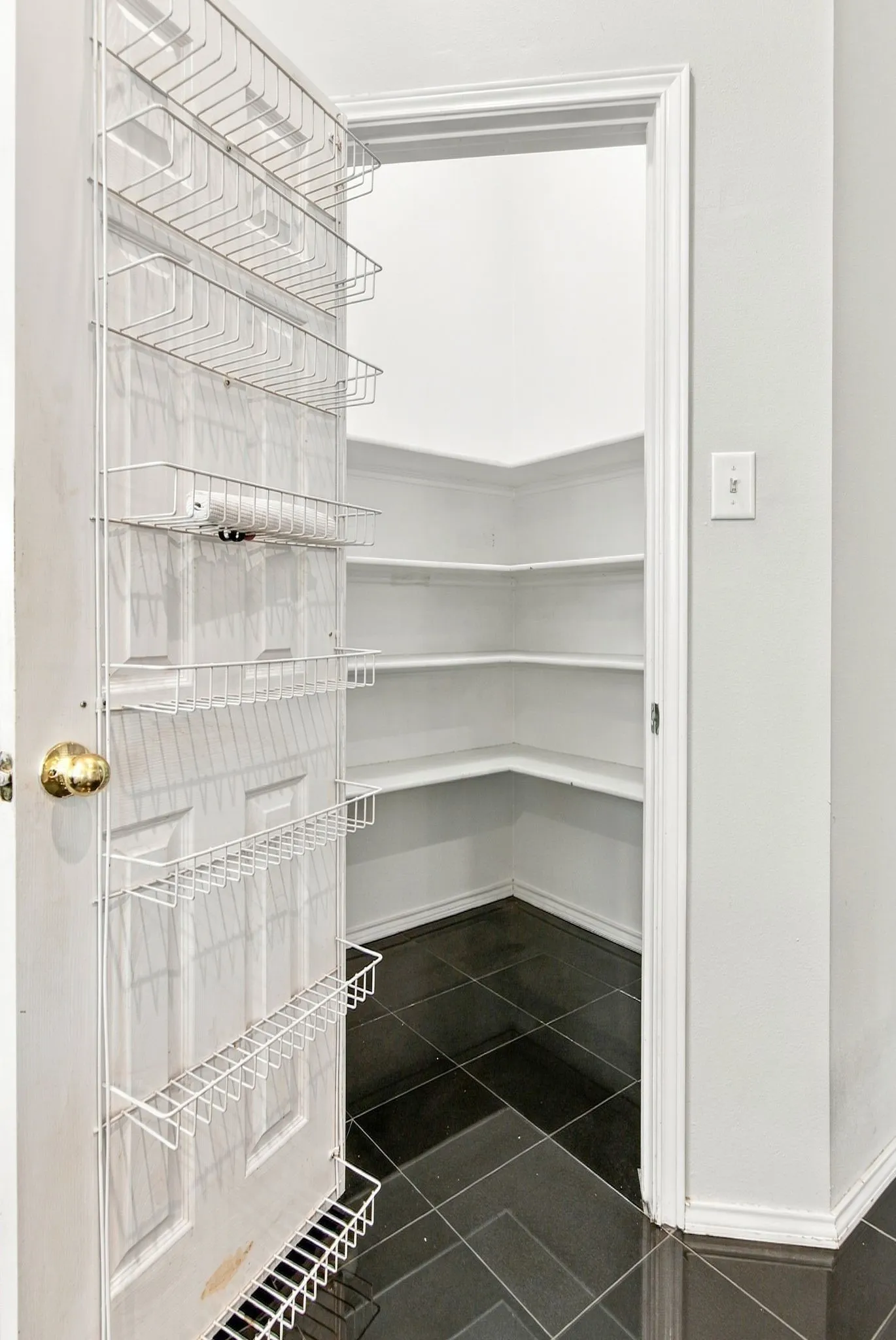 Walk-in pantry with wrap-around shelving, dark tile flooring, and additional door-mounted storage
