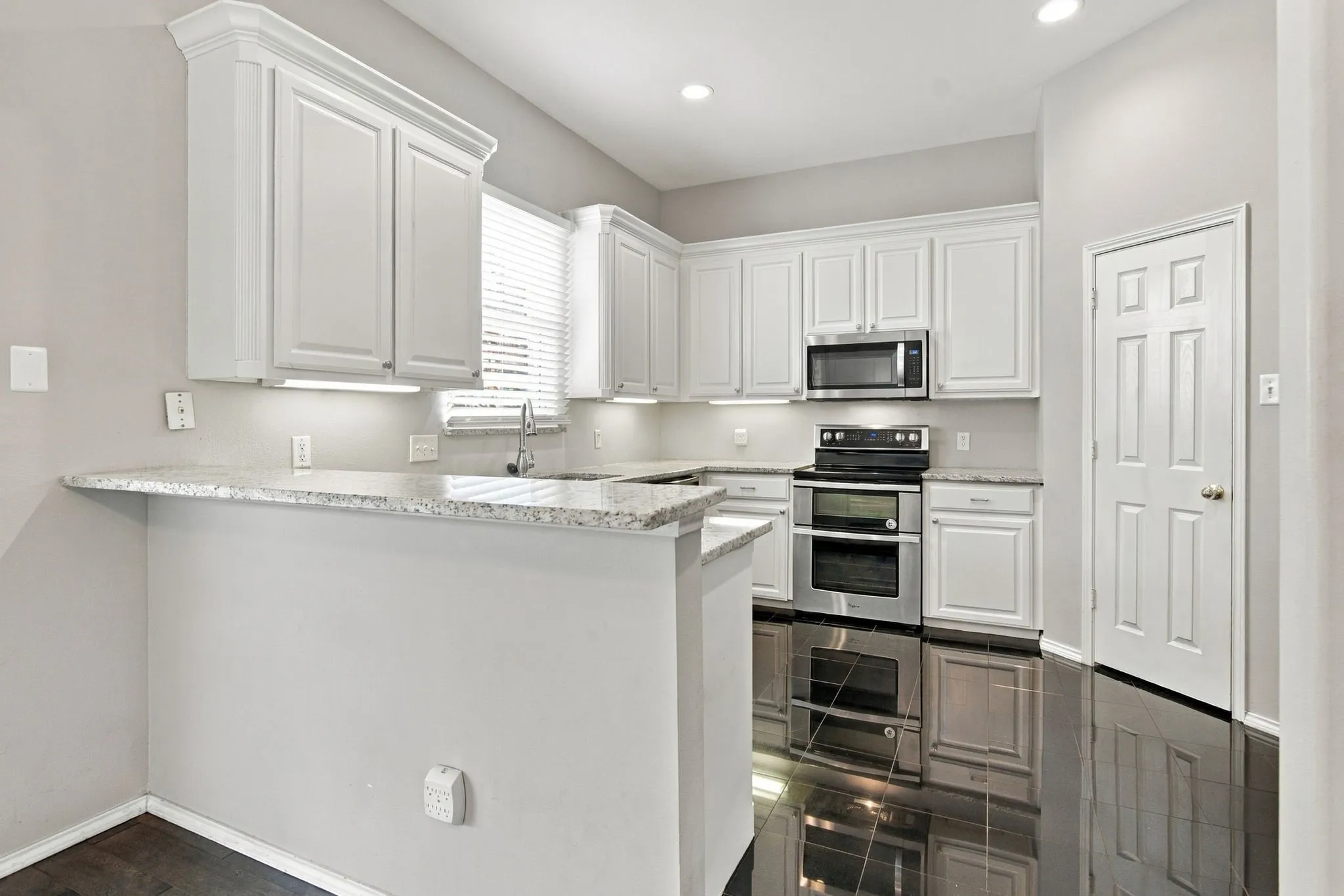 Kitchen featuring white cabinetry, light-toned countertops, stainless steel appliances, and dark tile flooring