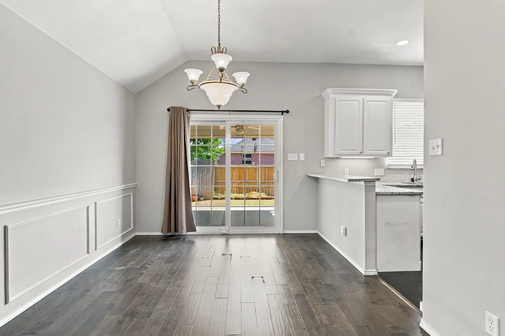 Vaulted ceiling with an elegant chandelier, wood-finish flooring, wainscoting detail, and a sliding glass door to the exterior