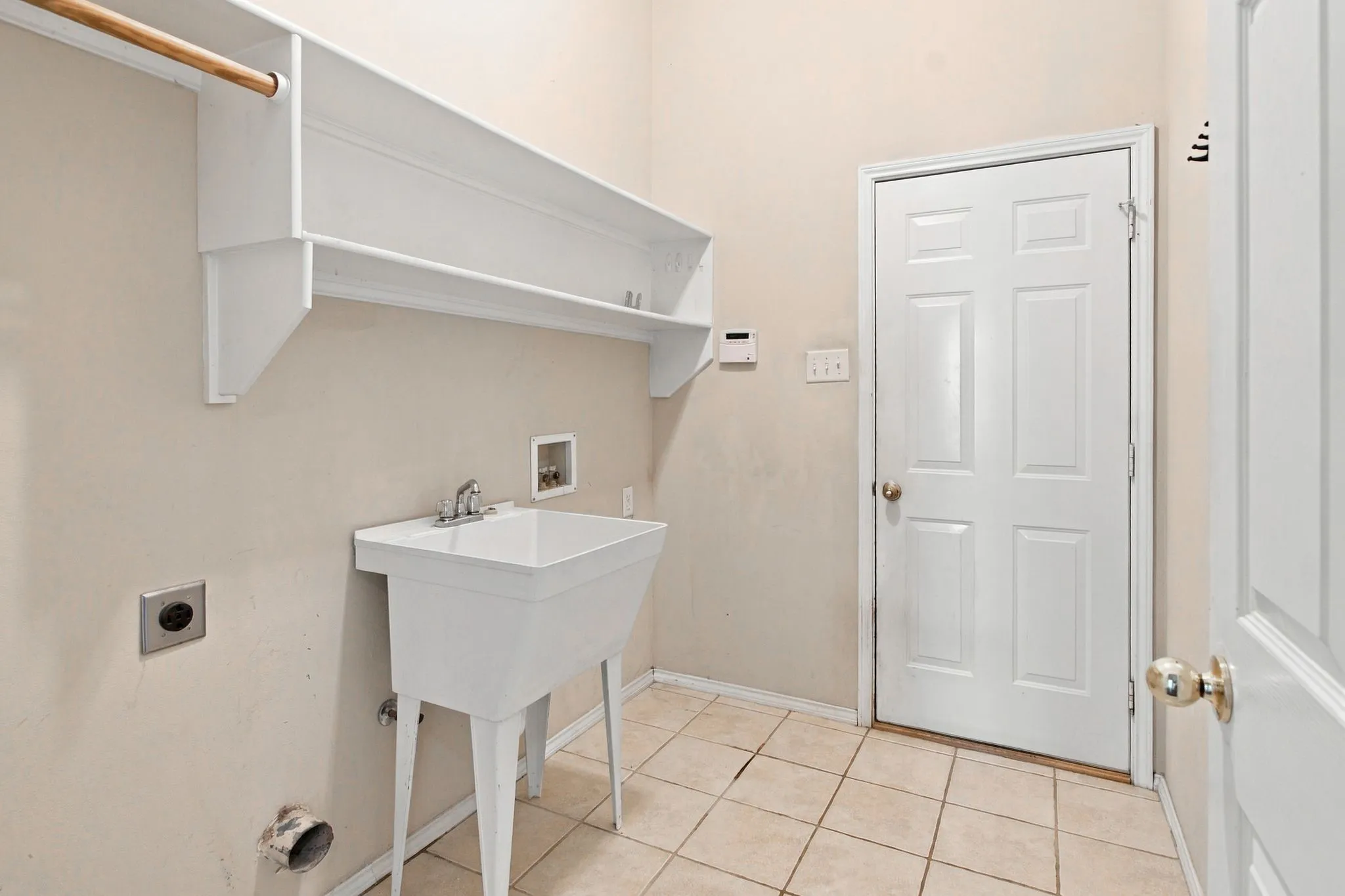 Utility room with a built-in utility sink, overhead shelving, clothes rod, and tile flooring