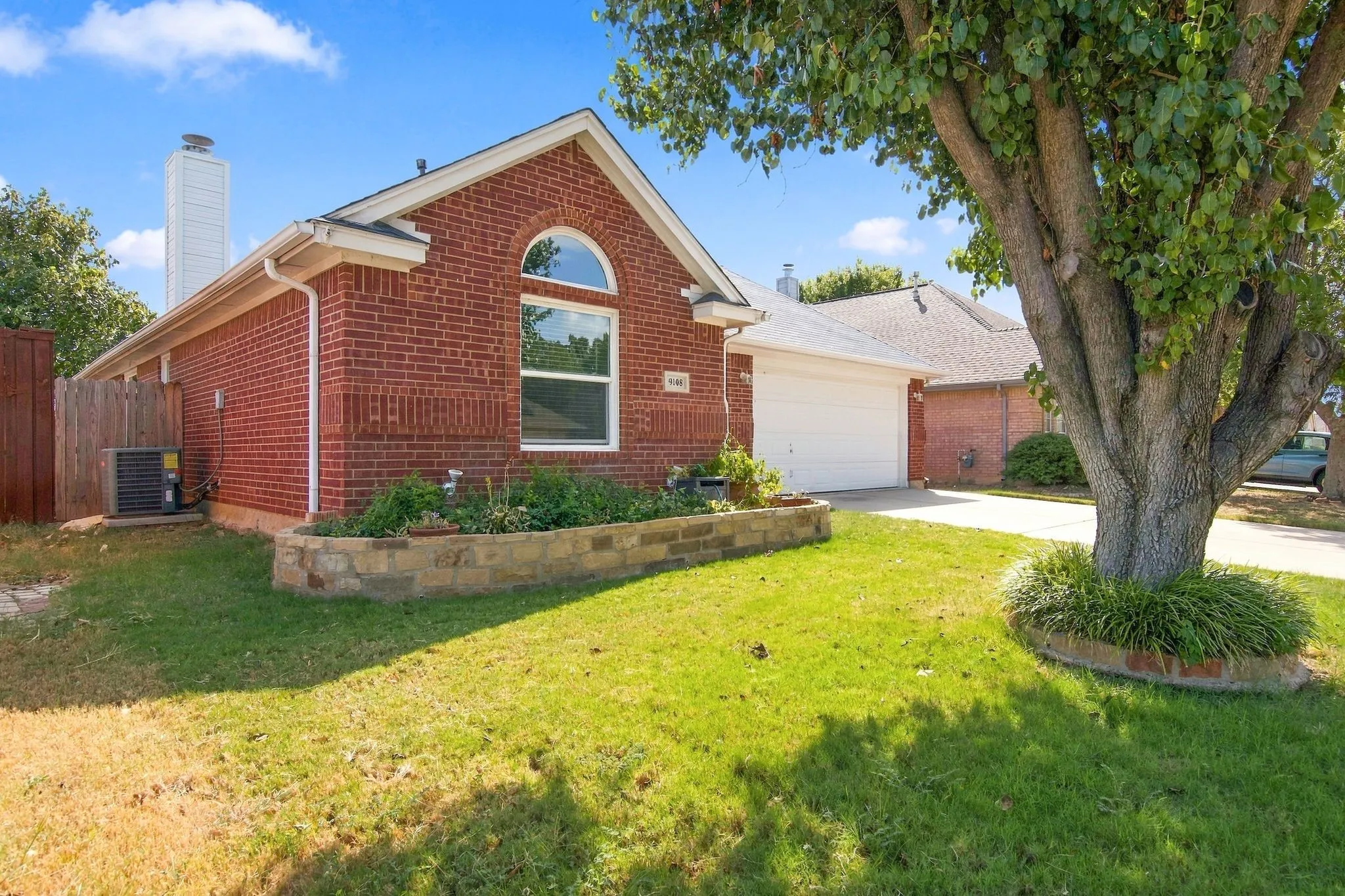Brick exterior with a prominent arched window, attached two-car garage, and a stone-faced planter bed