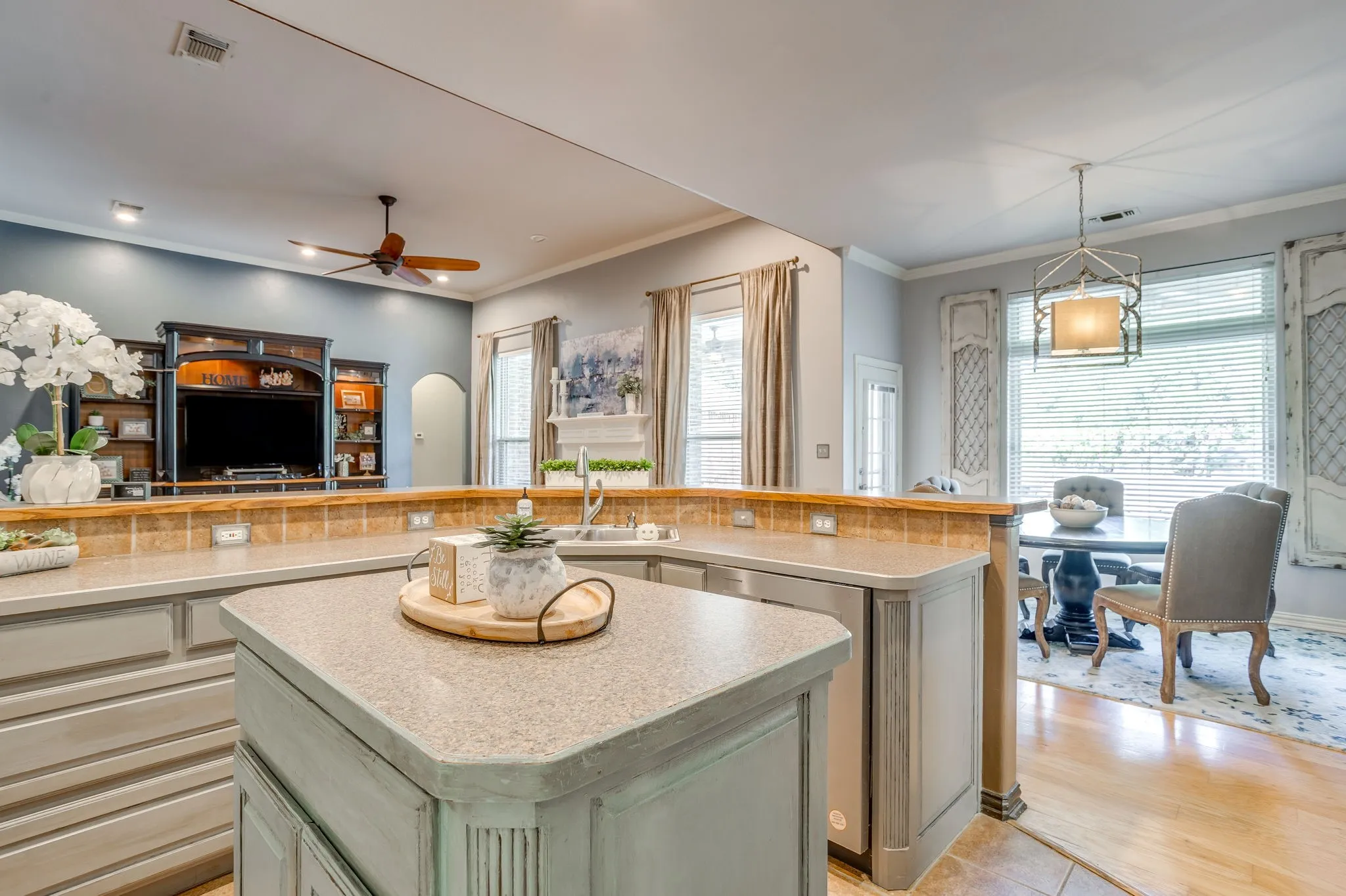 Kitchen island with integrated sink, stone-finish countertops, wood-finish cabinetry, and tile backsplash