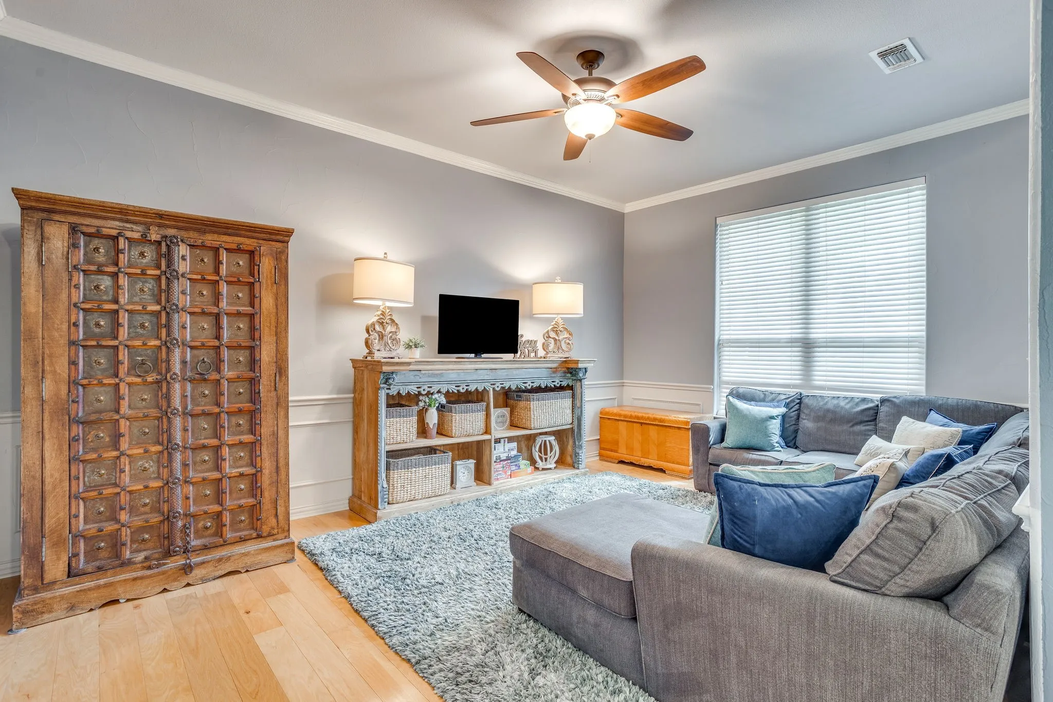 Second Living off entry with Crown molding, light wood-finish flooring, ceiling fan with integrated lighting, window with blinds, and wainscoting