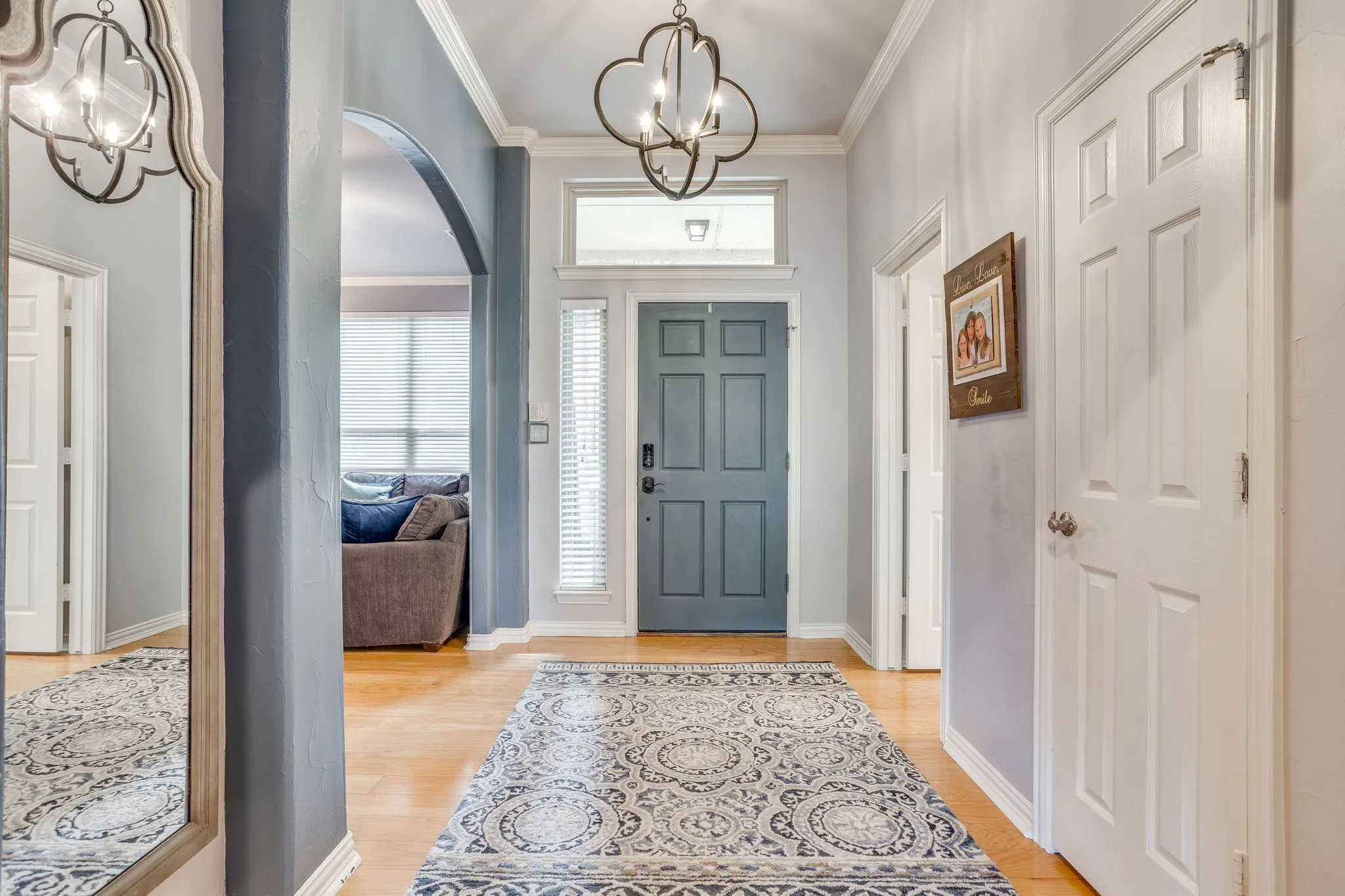 Hardwood-style flooring in the entry hall with crown molding, a decorative archway, a panel-style entry door, and a transom window