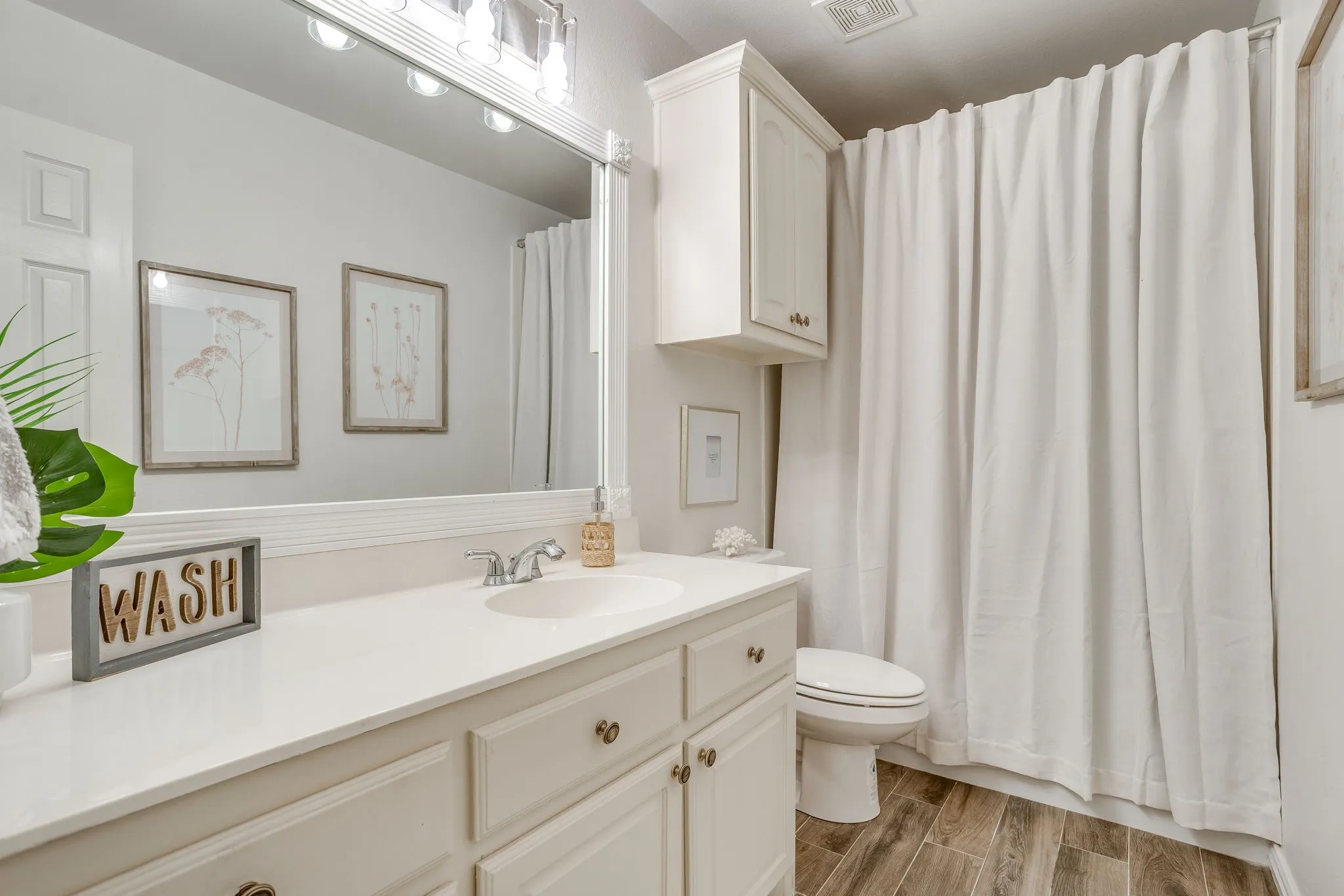 Shared bath for bedroom 3 & 4, vanity with integrated sink and storage cabinetry, illuminated mirror, wood-finish flooring, and wall-mounted storage cabinet