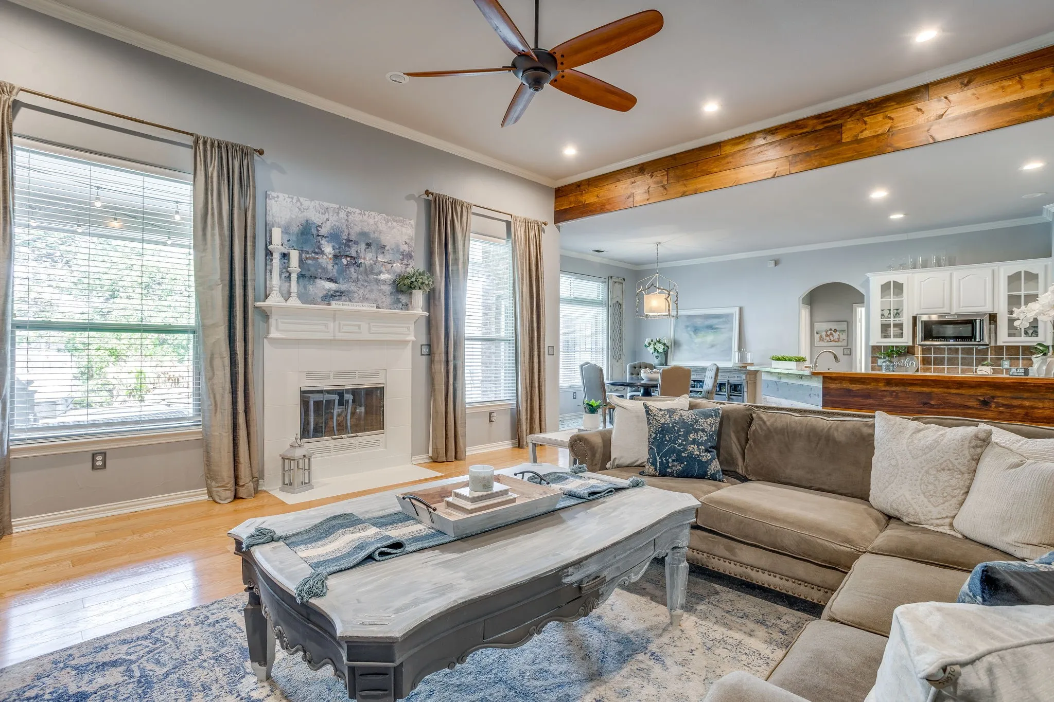 Wood-finish flooring, white fireplace with mantle, recessed lighting, wood ceiling fan, and exposed wood beam