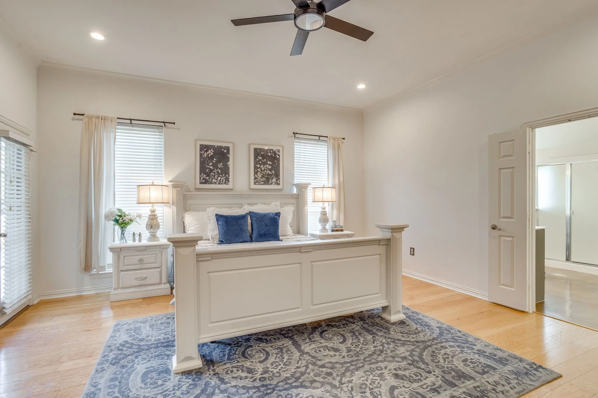 Primary bedroom with light wood-finish flooring, recessed lighting, and a dark-toned ceiling fan