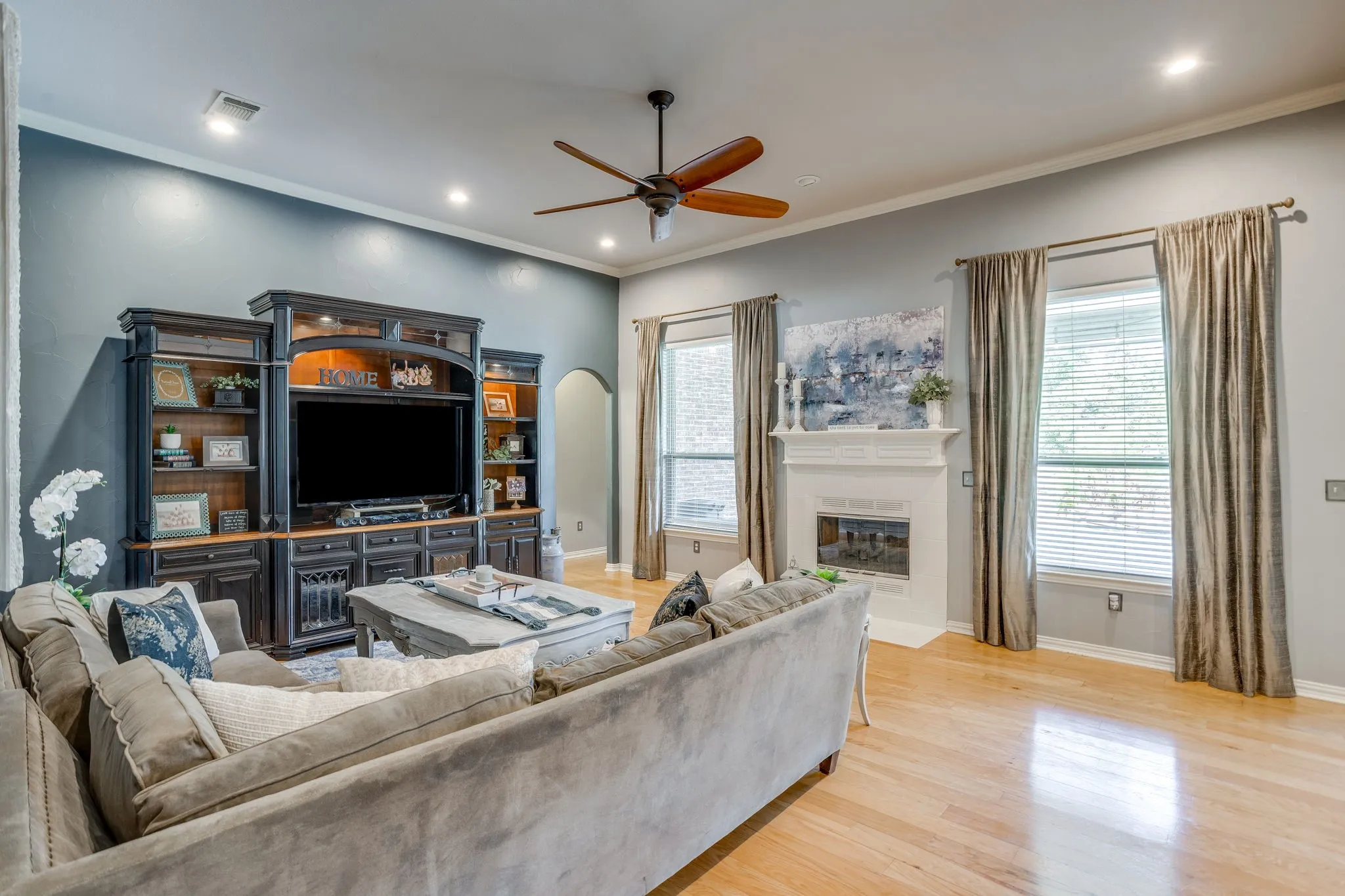Hardwood flooring, recessed lighting, ceiling fan, white mantel over fireplace, and multiple windows