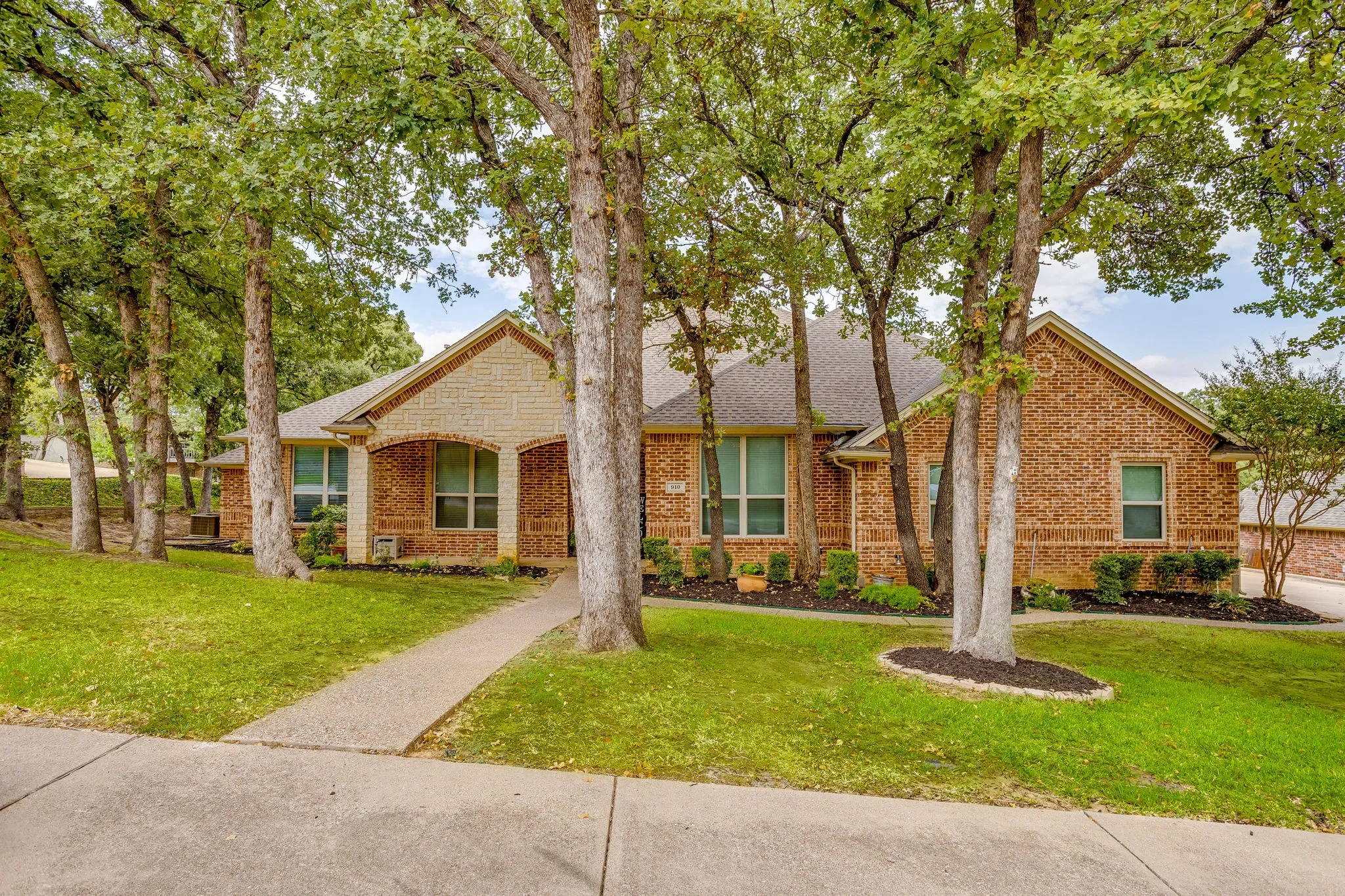 Brick exterior with stone accents, mature trees, manicured lawn, and a concrete pathway