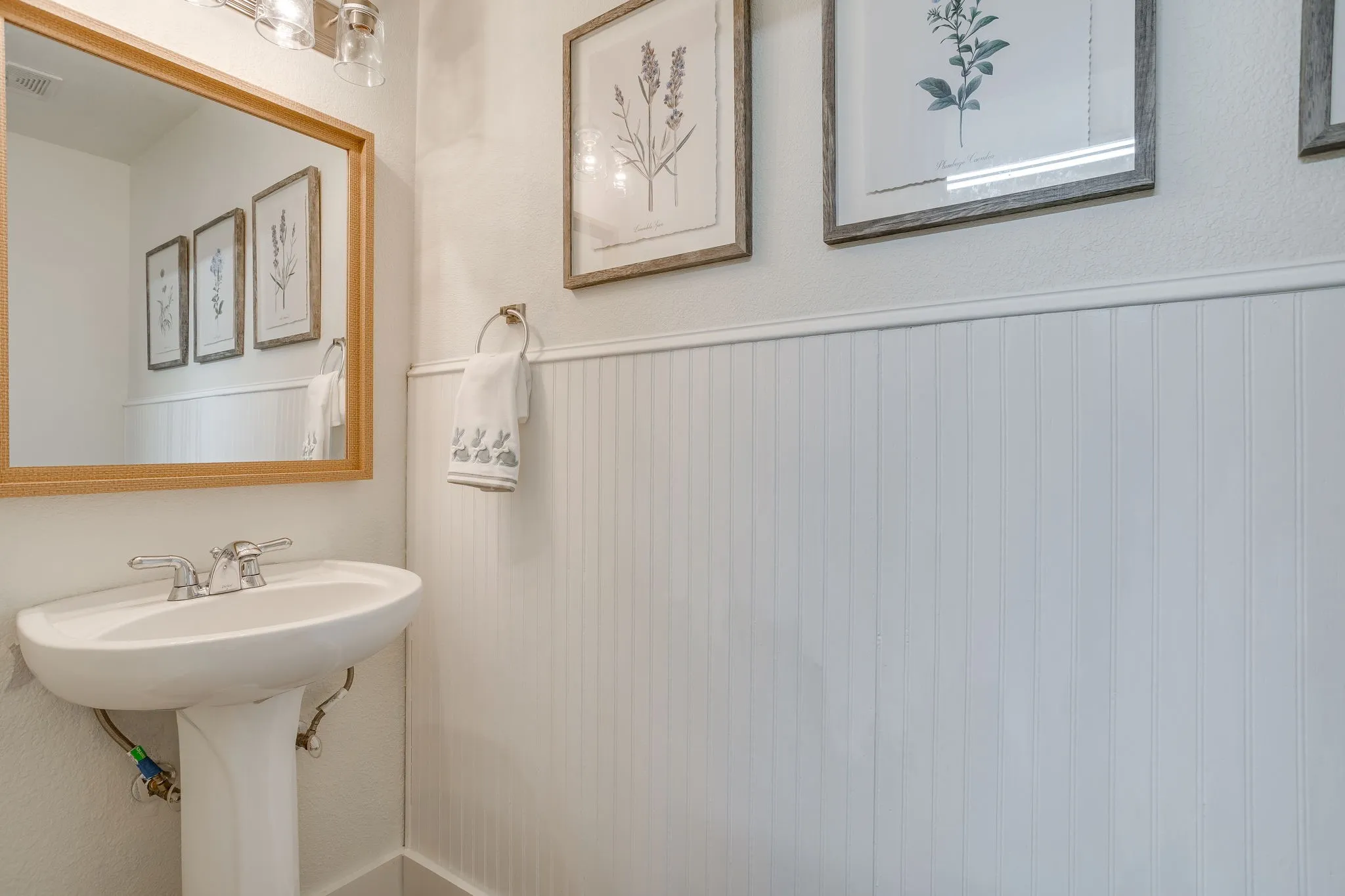 Half Bath off laundry room with Pedestal sink with chrome faucet, framed mirror, and beadboard wainscoting